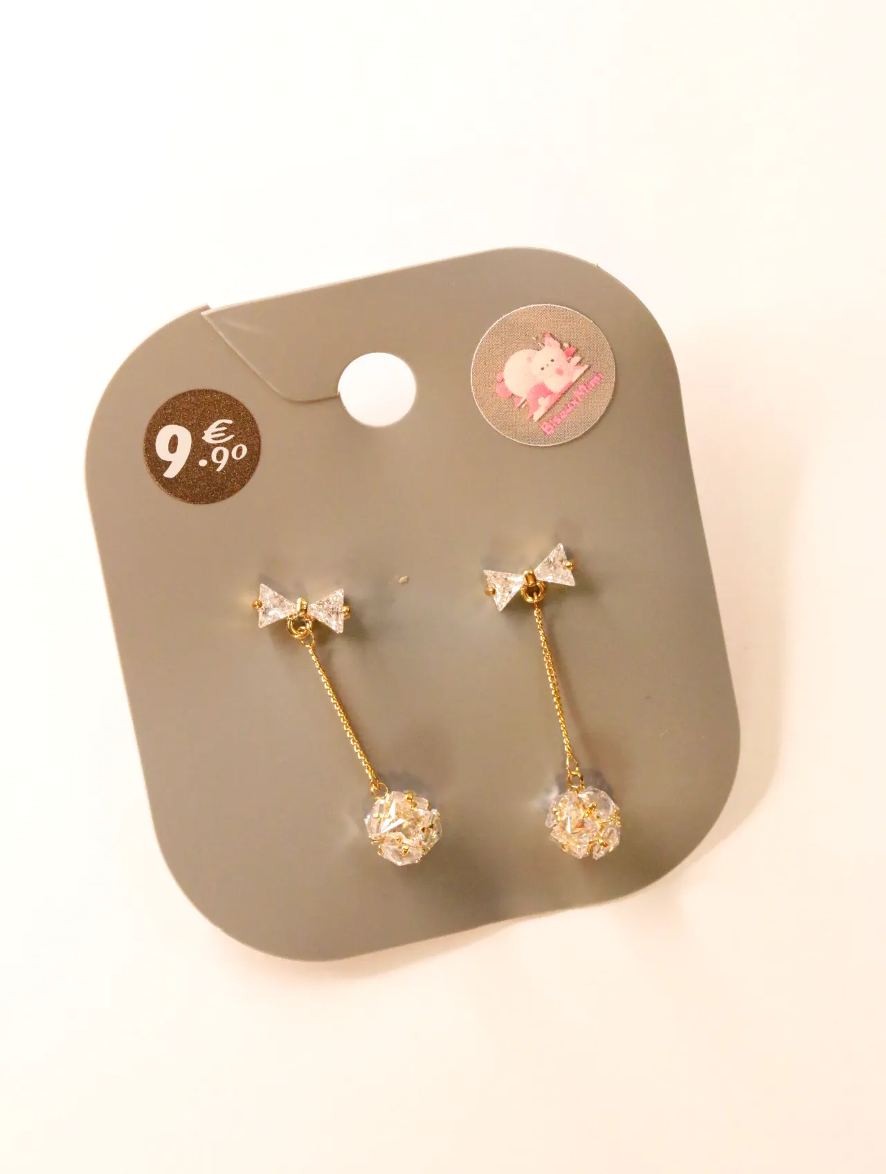 Pendientes largos dorados con lazos y bolas brillantes sobre tarjeta — pendientes para mujer, vista principal · Lola y Sol (24AE1243)