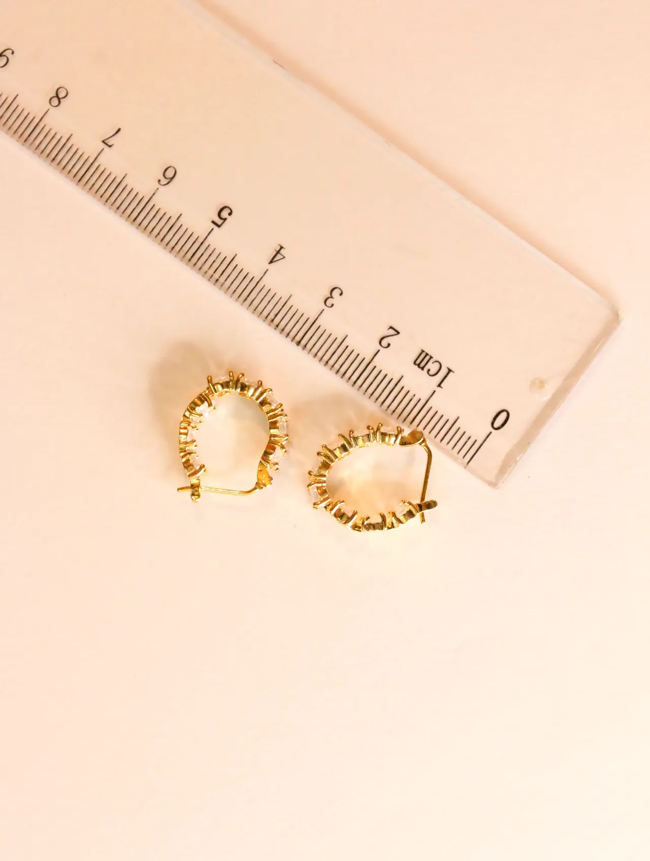 Pendientes ovalados de tono dorado junto a una regla — pendientes dorados, primer plano · Lola y Sol (24AE1247)