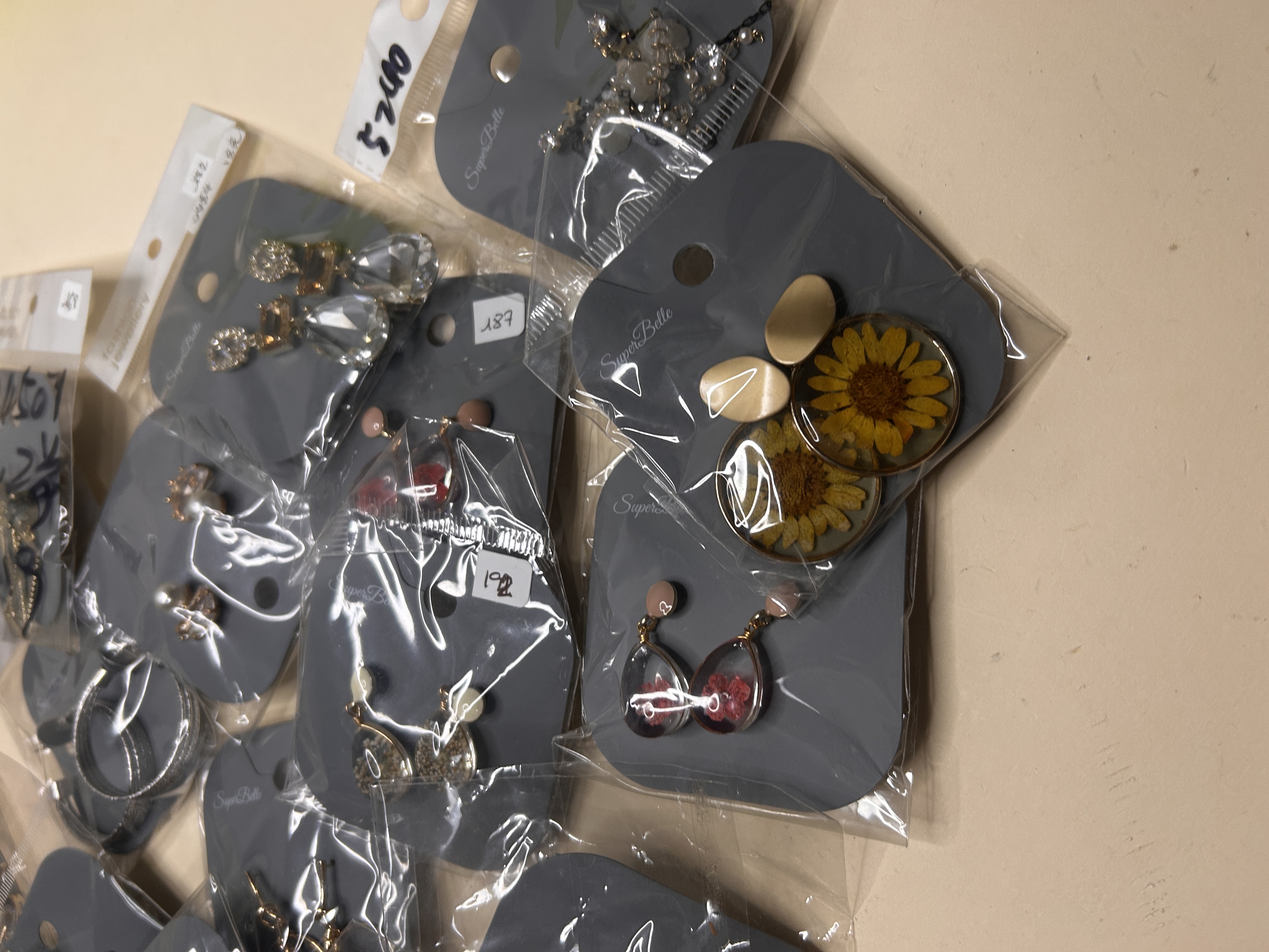 Primer plano de una variedad de pendientes de bisutería, empaquetados individualmente en tarjetas grises, mostrando diseños como girasoles y gemas en forma de lágrima transparente.
