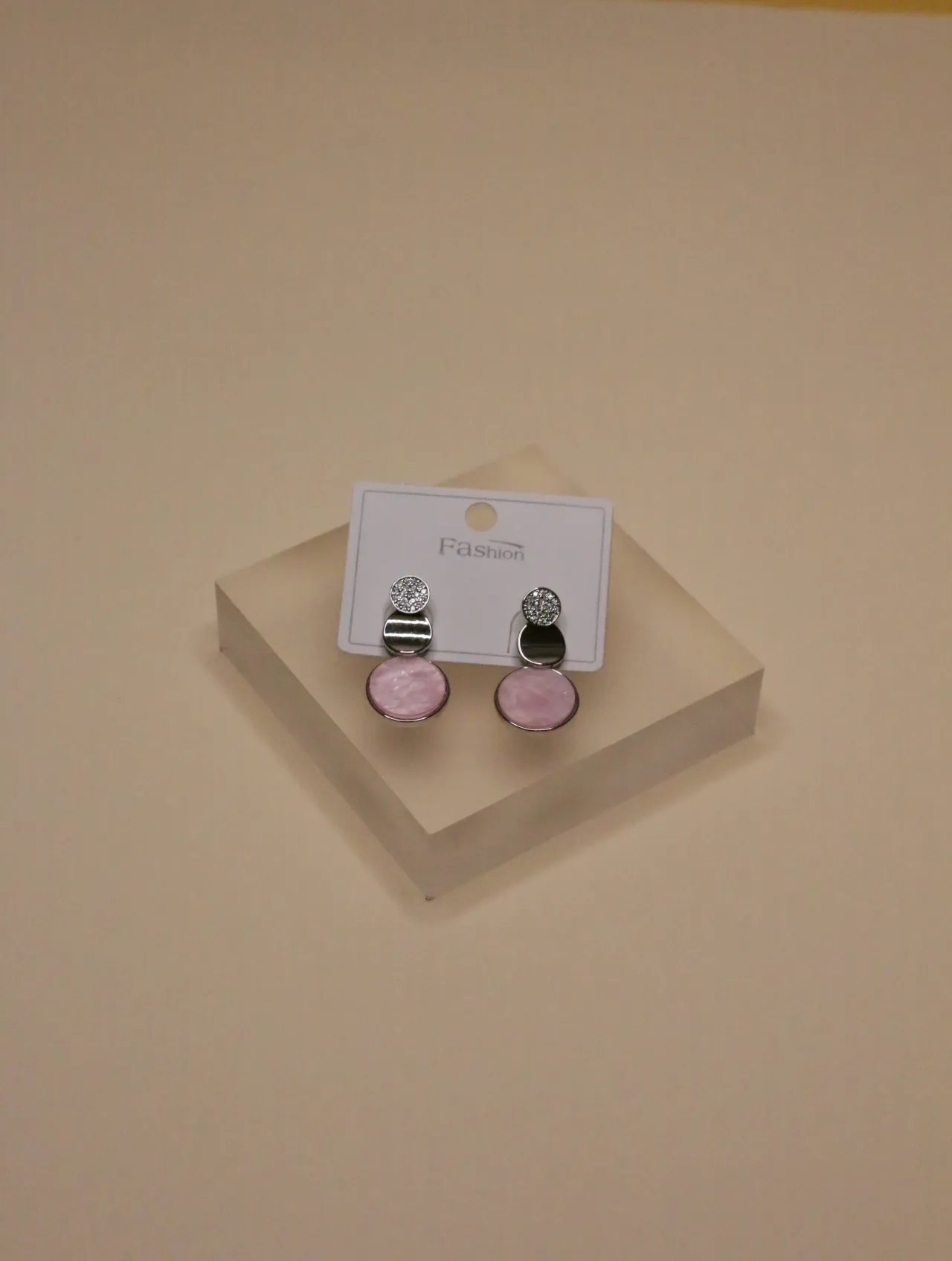 Primer plano de un par de pendientes colgantes esmaltados en rosa sobre un bloque de exhibición blanco, resaltando los detalles del diseño.