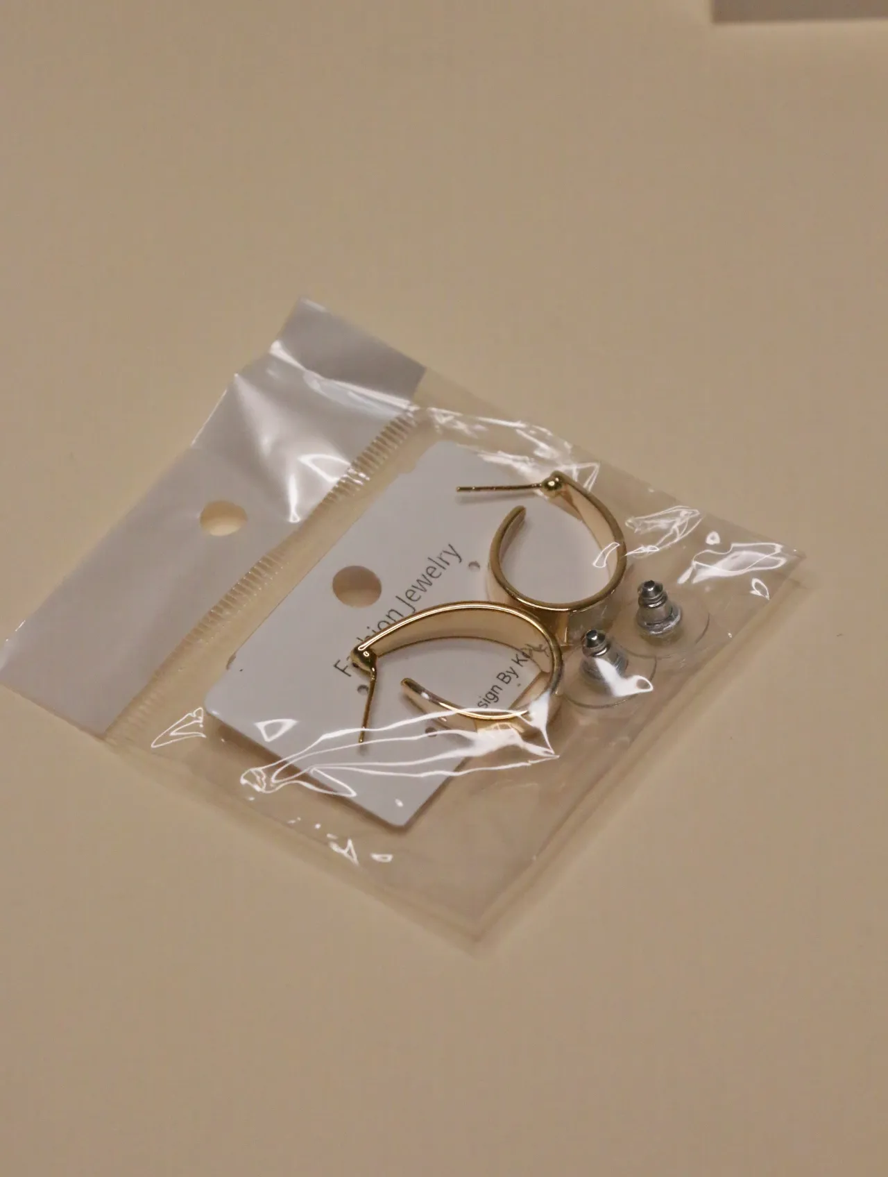 Par individual de pendientes de aro dorados con cierres de mariposa, aún en bolsa de plástico transparente.