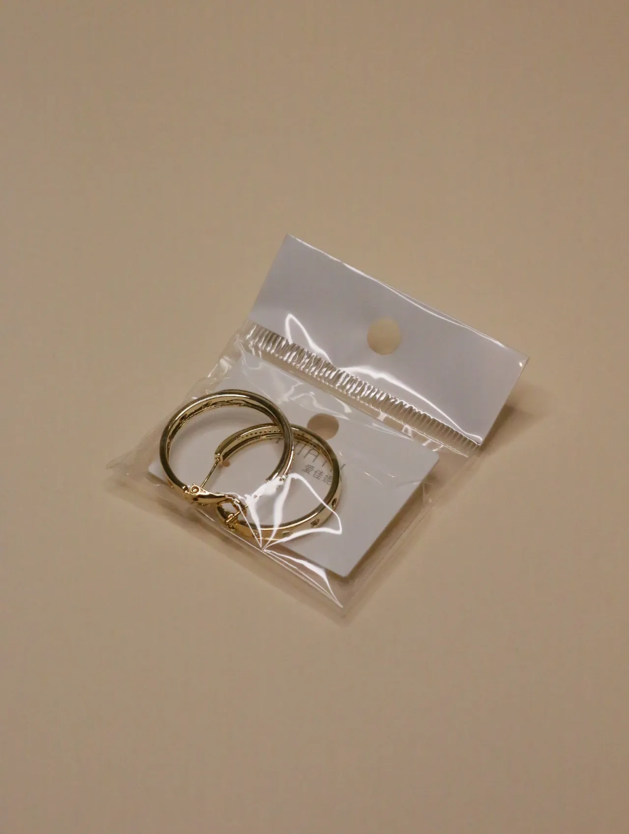 Primer plano de un par de pendientes de aro dorados en su empaque de venta, mostrando su diseño simple.