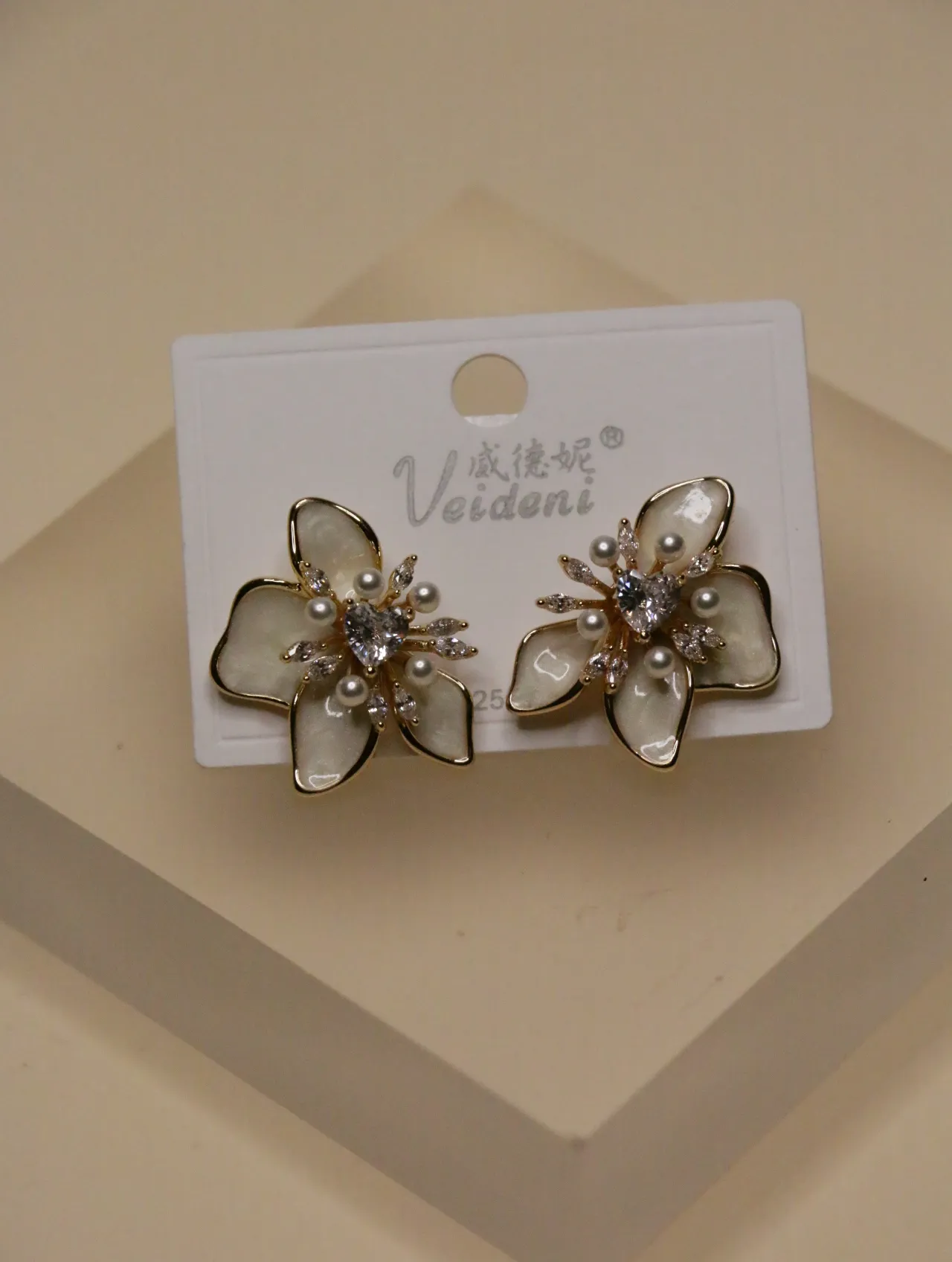 Primer plano de un par de elegantes pendientes de flor blanca con detalles de perlas y cristales sobre una tarjeta de exhibición