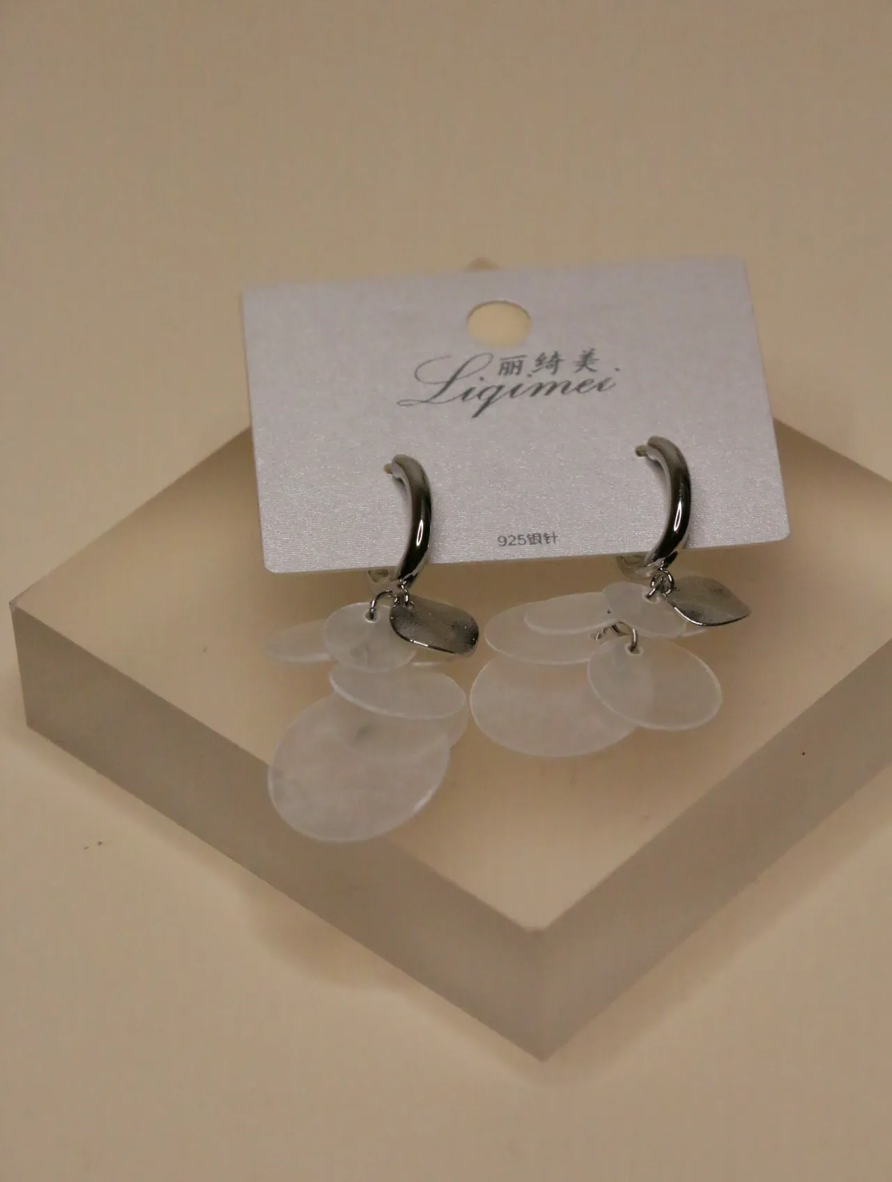 Vista frontal de pendientes de aro con caída estilo nácar blanco sobre un bloque expositor.