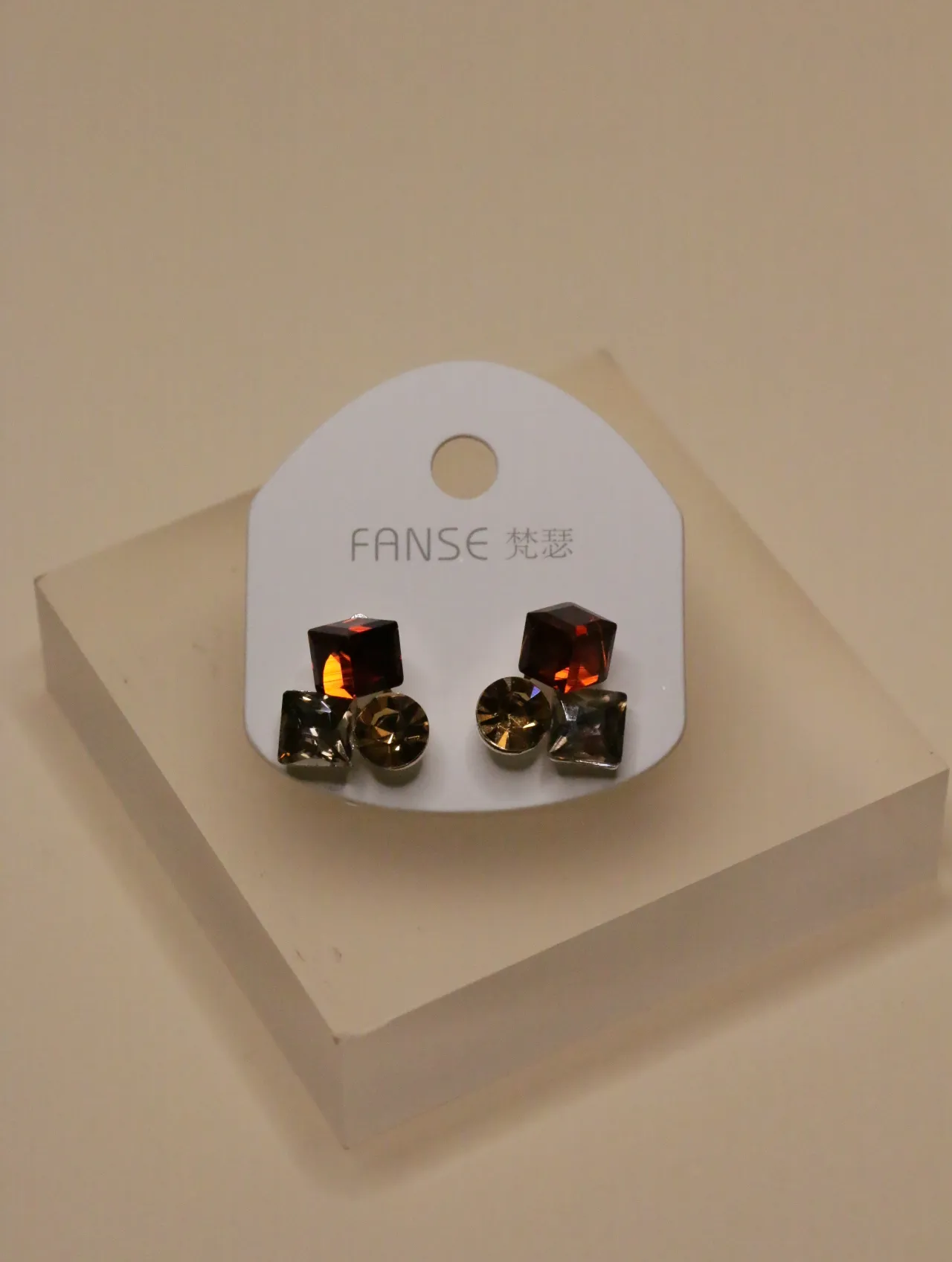 Pendientes de tachuela geométricos con joyas rojas y marrones sobre una tarjeta blanca.