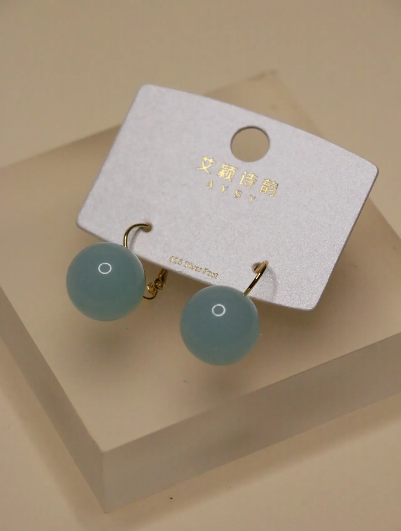 Primer plano de un par de pendientes de esfera azul pastel en una tarjeta de presentación blanca