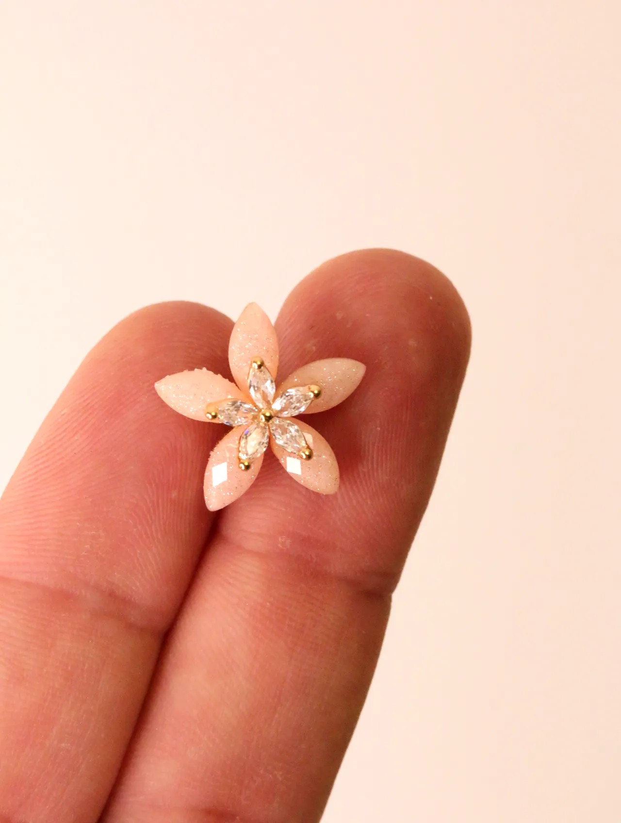 Primer plano de un único pendiente de botón de flor rosa sostenido entre los dedos — pendientes de moda, vista lateral · Lola y Sol (BO-PD-032)