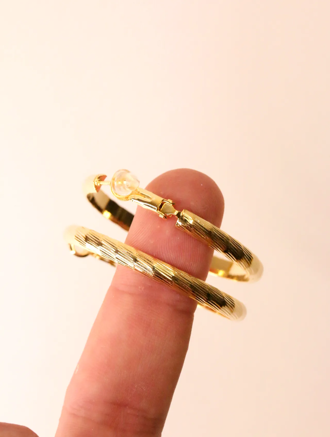 Primer plano de un dedo sosteniendo un pendiente de aro dorado texturizado, resaltando el mecanismo de cierre. — pendientes de moda, vista lateral · Lol…