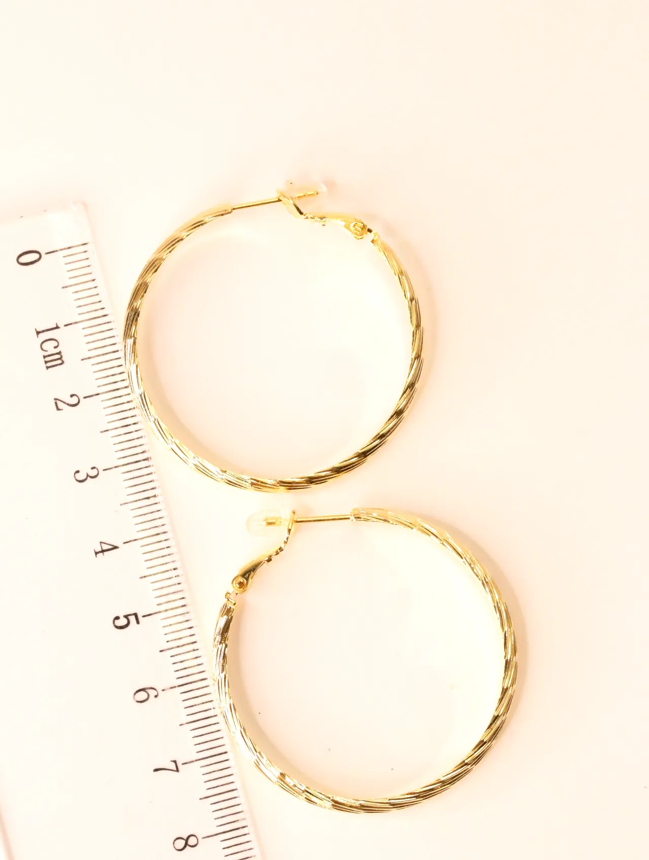 Pendientes de aro dorados texturizados junto a una regla, indicando su tamaño aproximado. — pendientes originales, detalle del acabado · Lola y Sol (BO-…