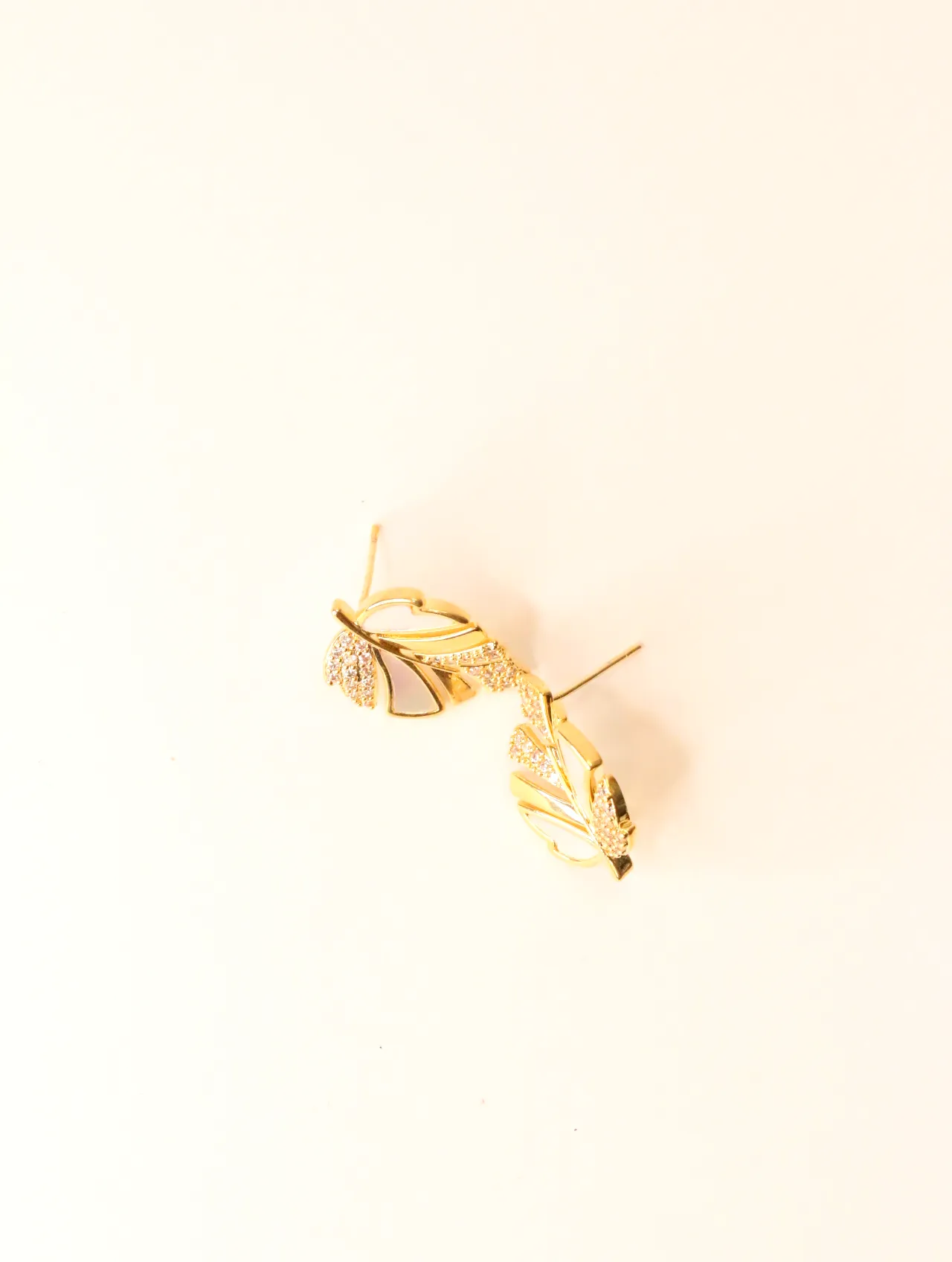 Par de pendientes de botón dorados con diseño de hoja, nácar blanco y acentos de circonita sobre fondo blanco, vistos en ángulo. — pendientes baratos, d…