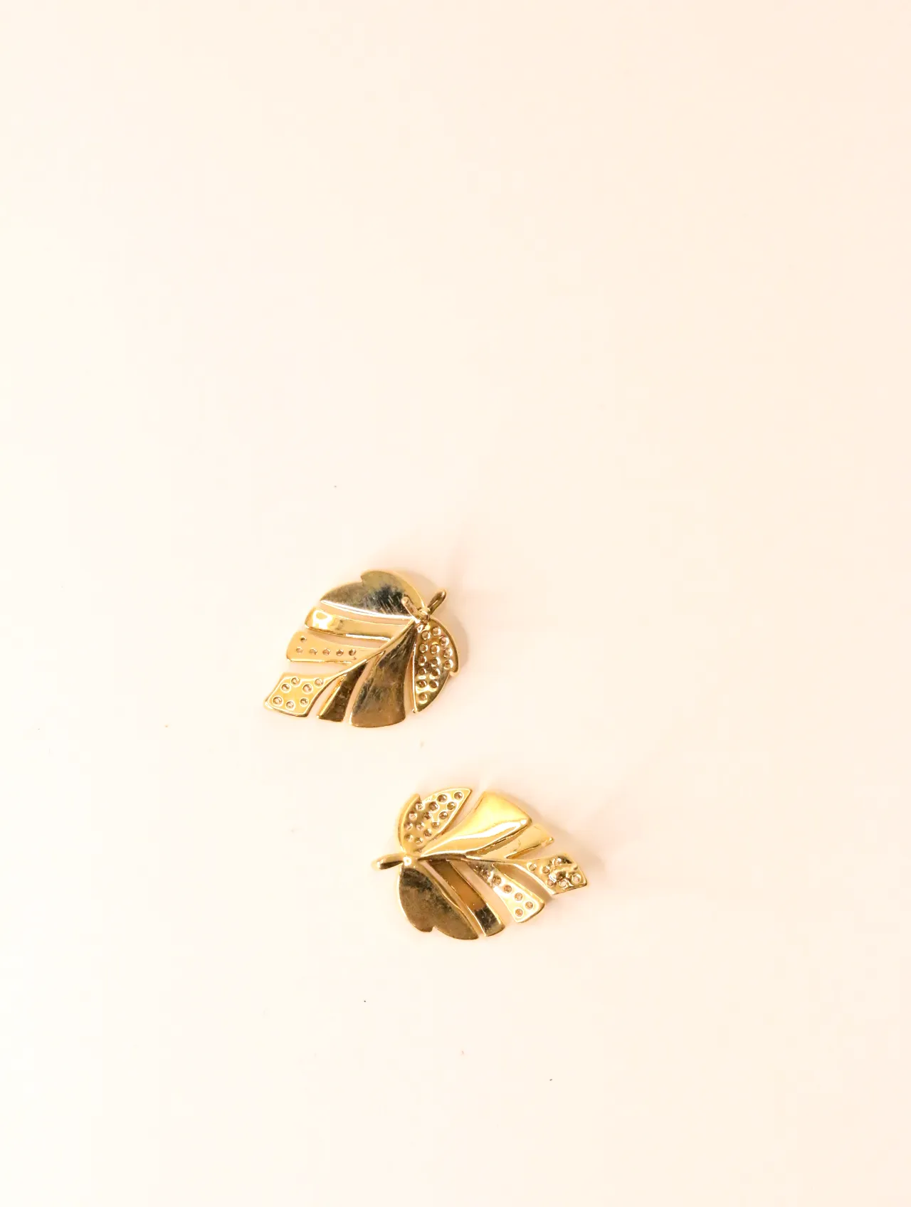 Vista superior de dos pendientes de botón dorados con diseño de hoja y superficie texturizada sobre fondo blanco. — pendientes de moda, vista lateral ·…