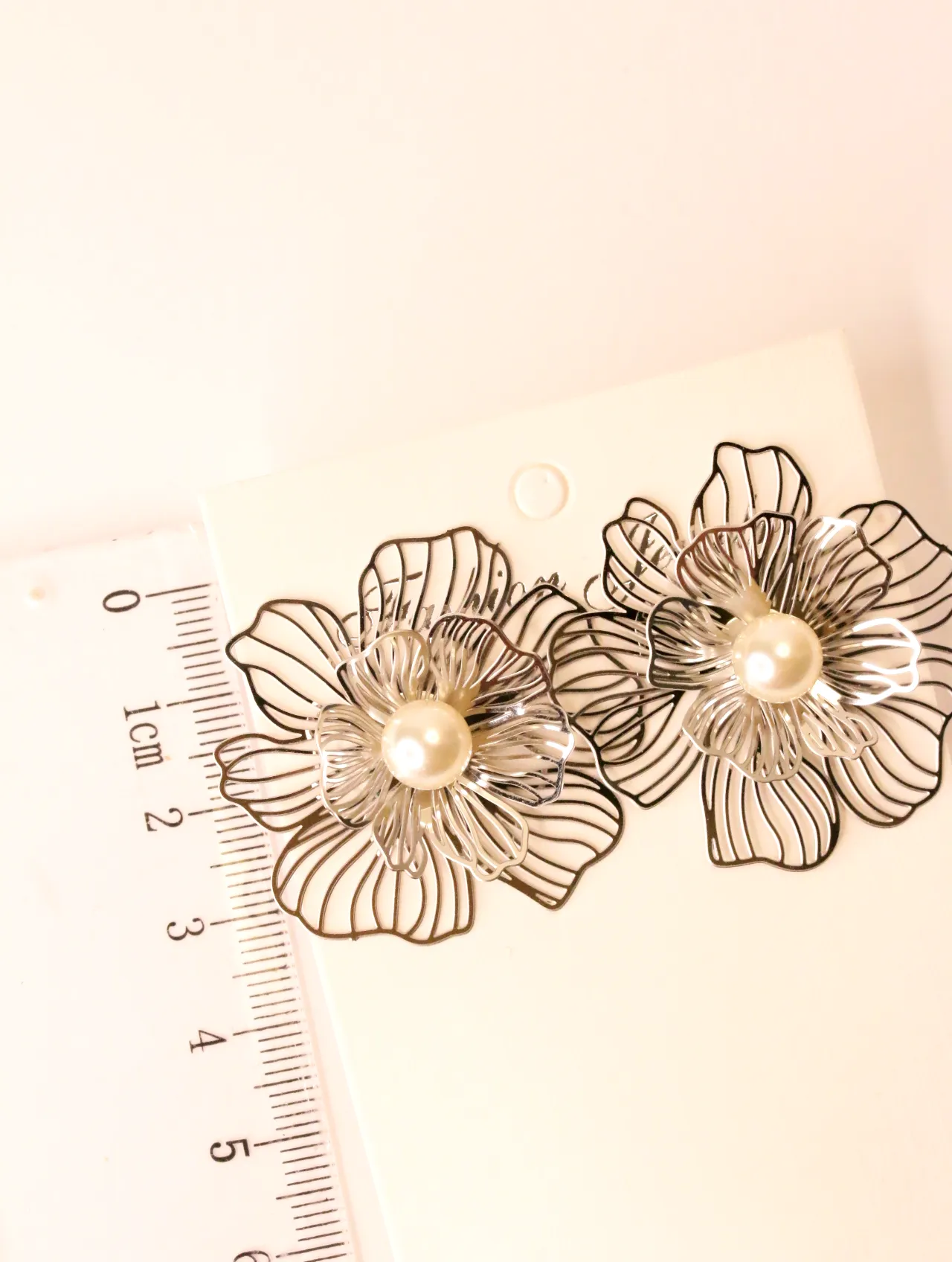 Par de pendientes florales con perla en una tarjeta junto a una regla para escala. — pendientes de moda, vista lateral · Lola y Sol (BO-PD-038)