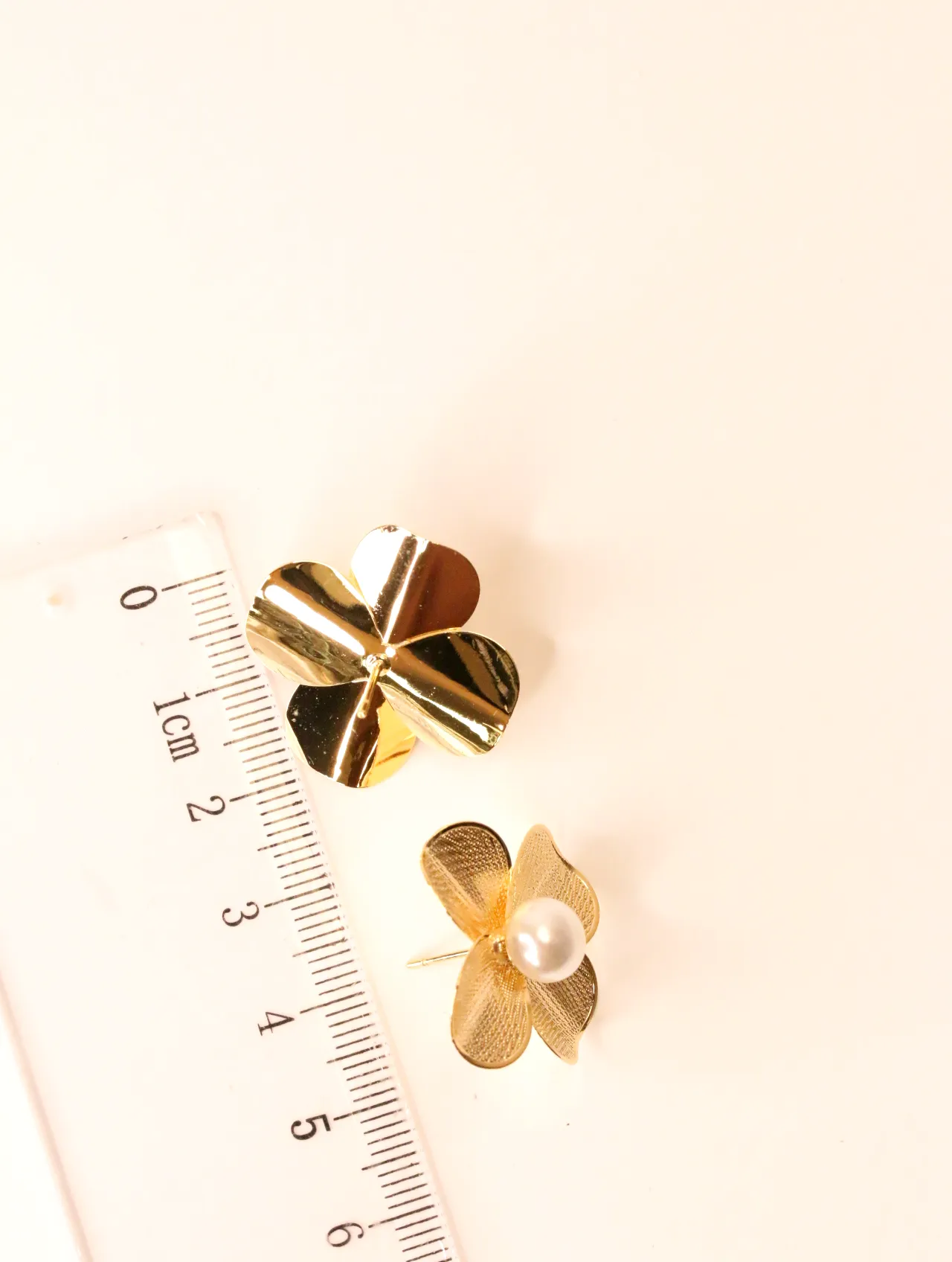 Pendiente de flor dorada con perla junto a una regla para escala — pendientes de moda, vista lateral · Lola y Sol (BO-PD-039)