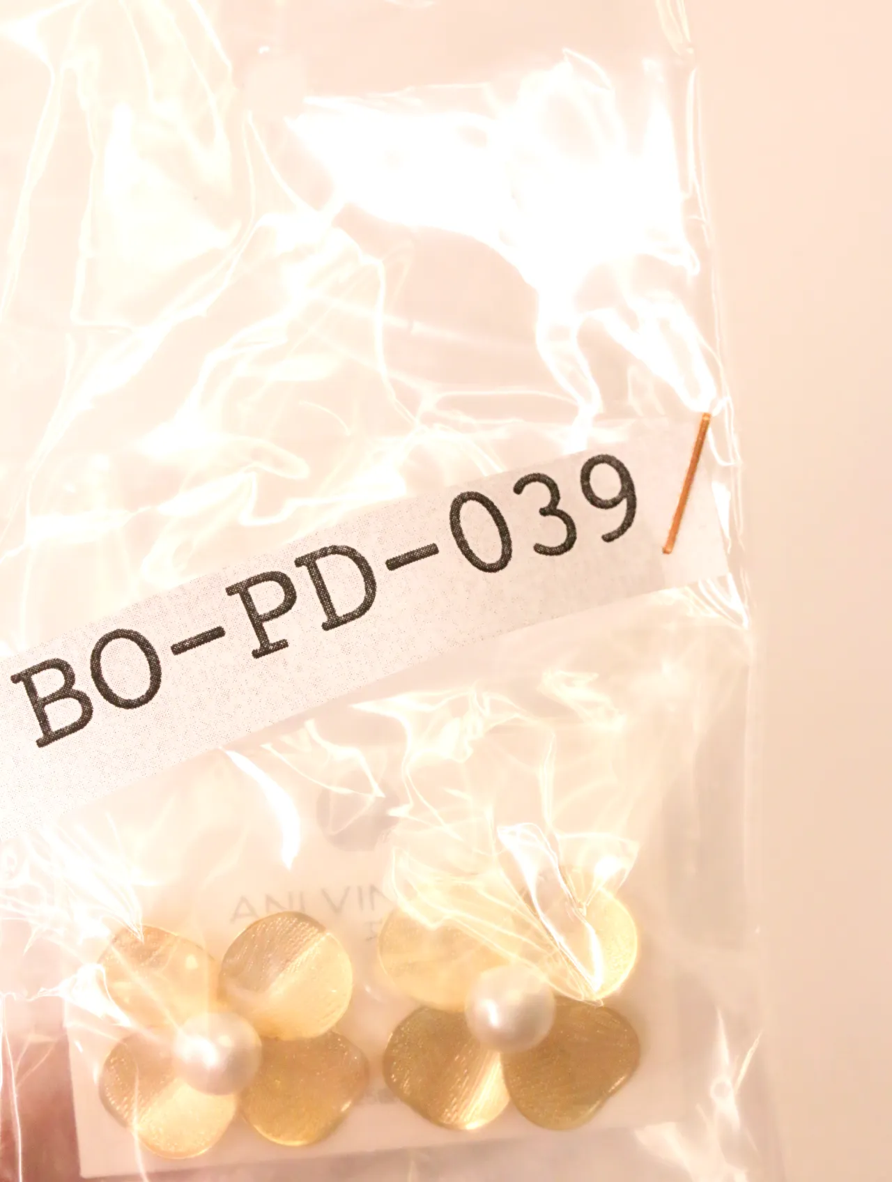 Pendientes de flor dorada con perlas sellados en una bolsa de plástico transparente con etiqueta de referencia — pendientes originales, detalle del acab…