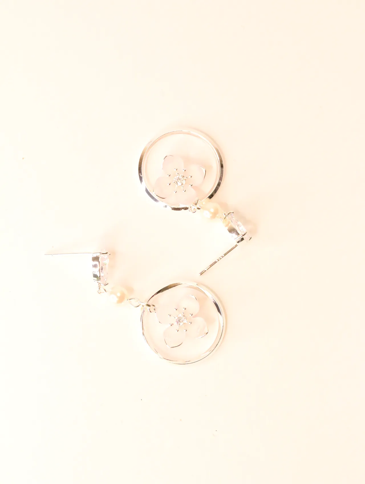 Vista superior de dos pendientes de aro plateados con detalles de flor rosa, sobre una superficie clara. — pendientes baratos, detalle · Lola y Sol (BO-…
