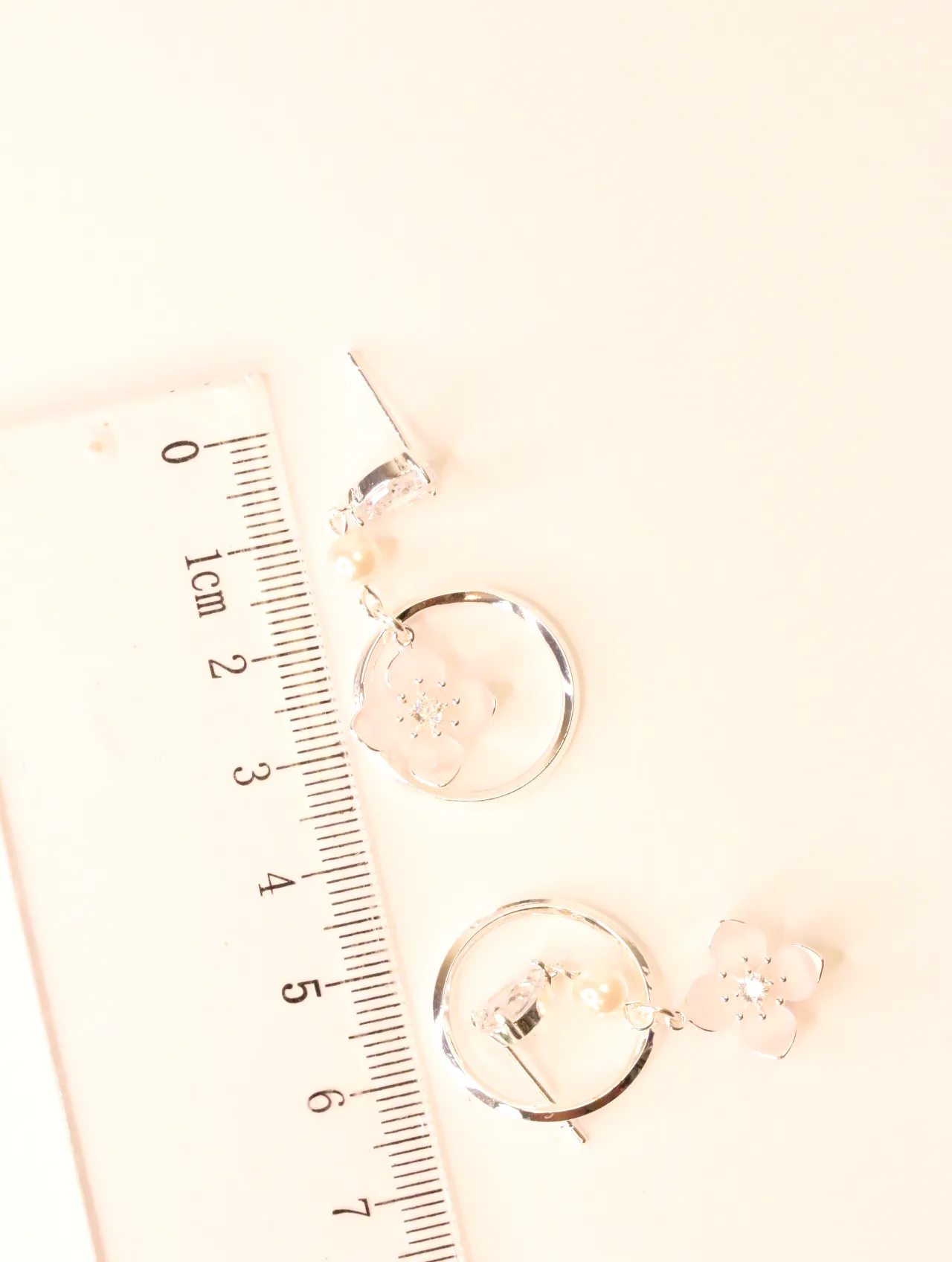 Pendientes de aro plateados con detalles de flor rosa, junto a una regla que muestra su tamaño. — pendientes dorados, primer plano · Lola y Sol (BO-PD-041)