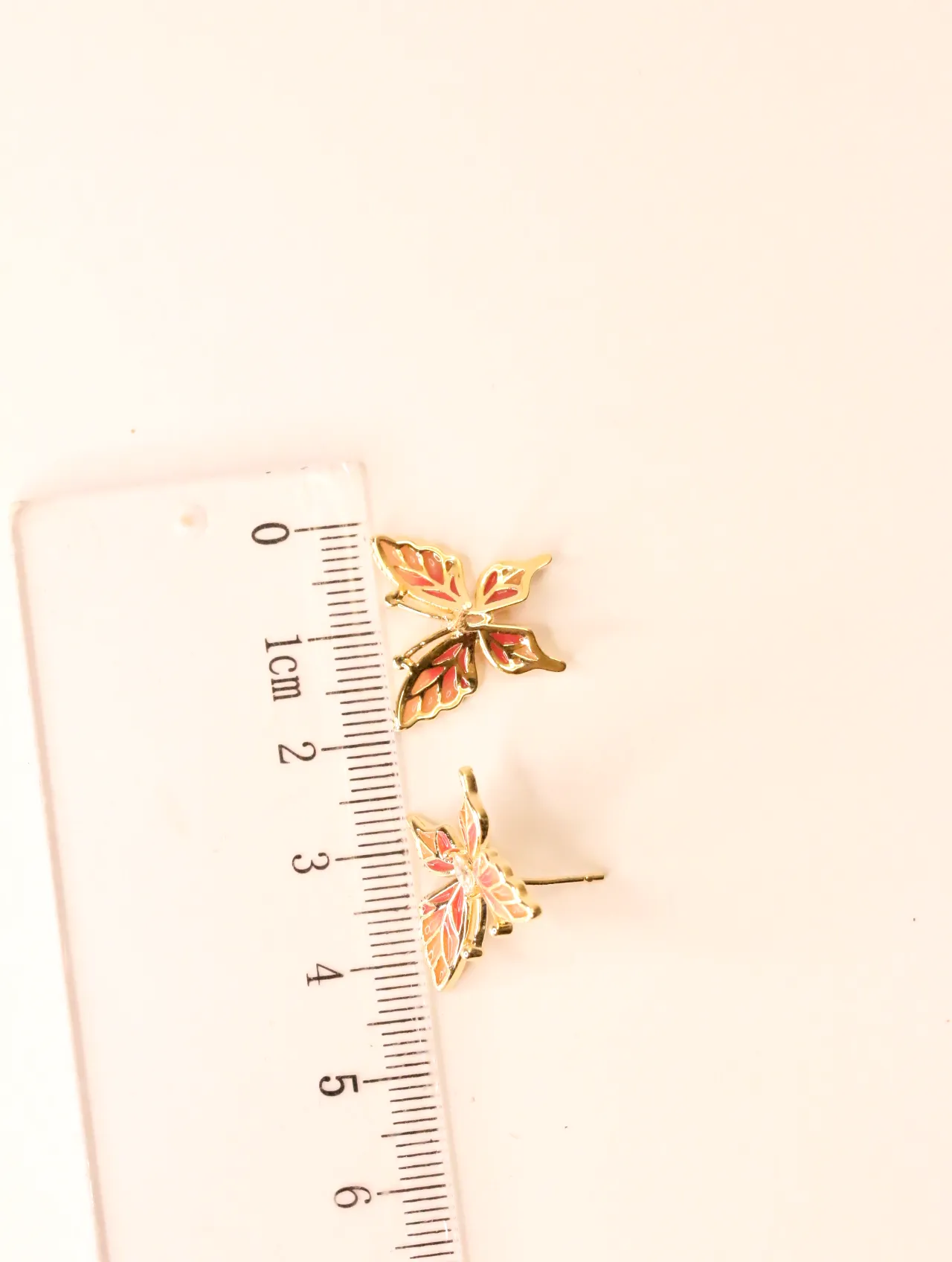 Par de pequeños pendientes de botón con forma de mariposa junto a una regla, mostrando el tamaño. — pendientes baratos, detalle · Lola y Sol (BO-PD-042)