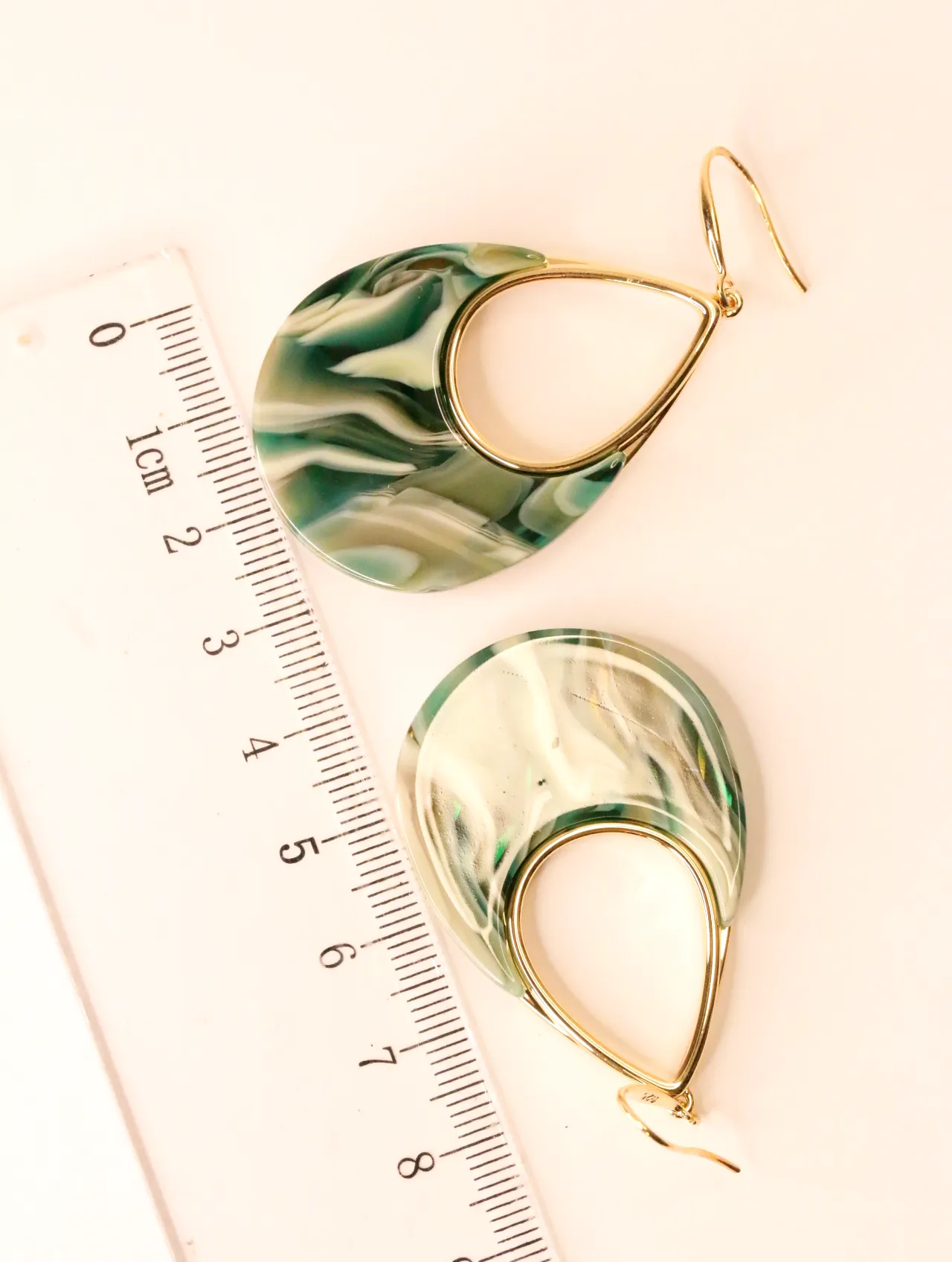 Par de pendientes largos con diseño de remolinos verdes y blancos junto a una regla para escala. — pendientes originales, detalle del acabado · Lola y S…