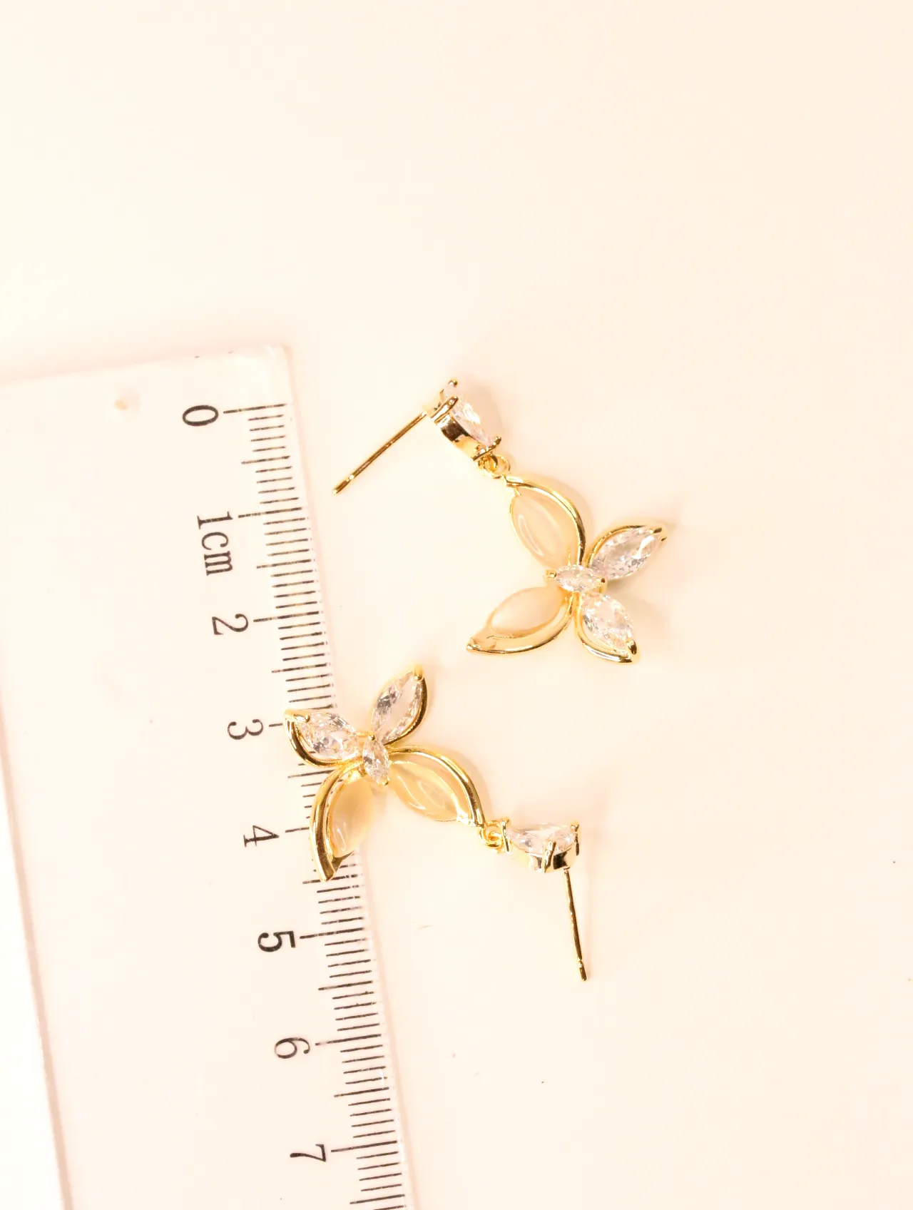 Pendientes de mariposa colgantes junto a una regla para escala — pendientes de moda, vista lateral · Lola y Sol (BO-PD-044)