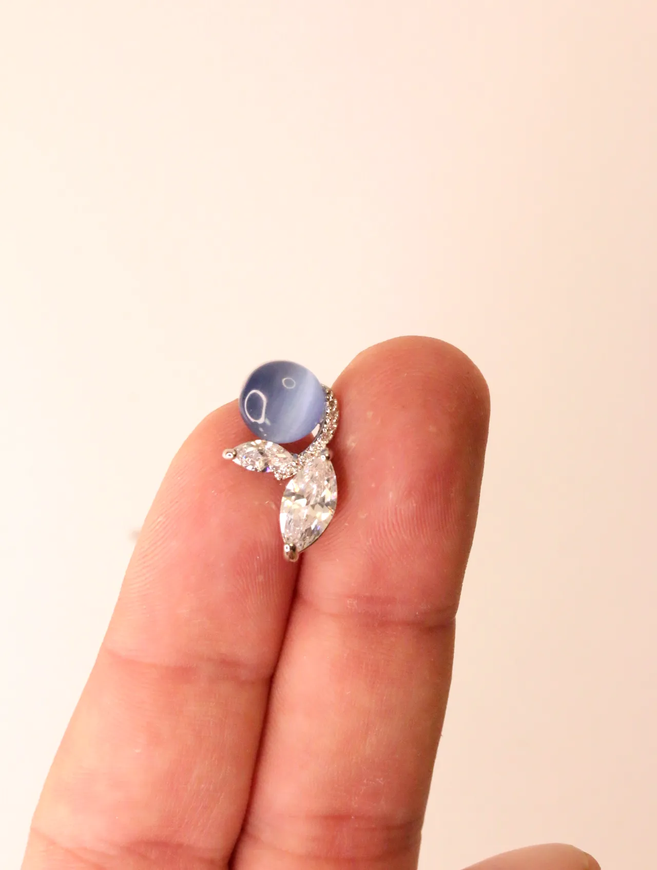 Primer plano de un solo pendiente con piedra azul y circonitas brillantes sobre un dedo, mostrando el detalle — pendientes dorados, primer plano · Lola…