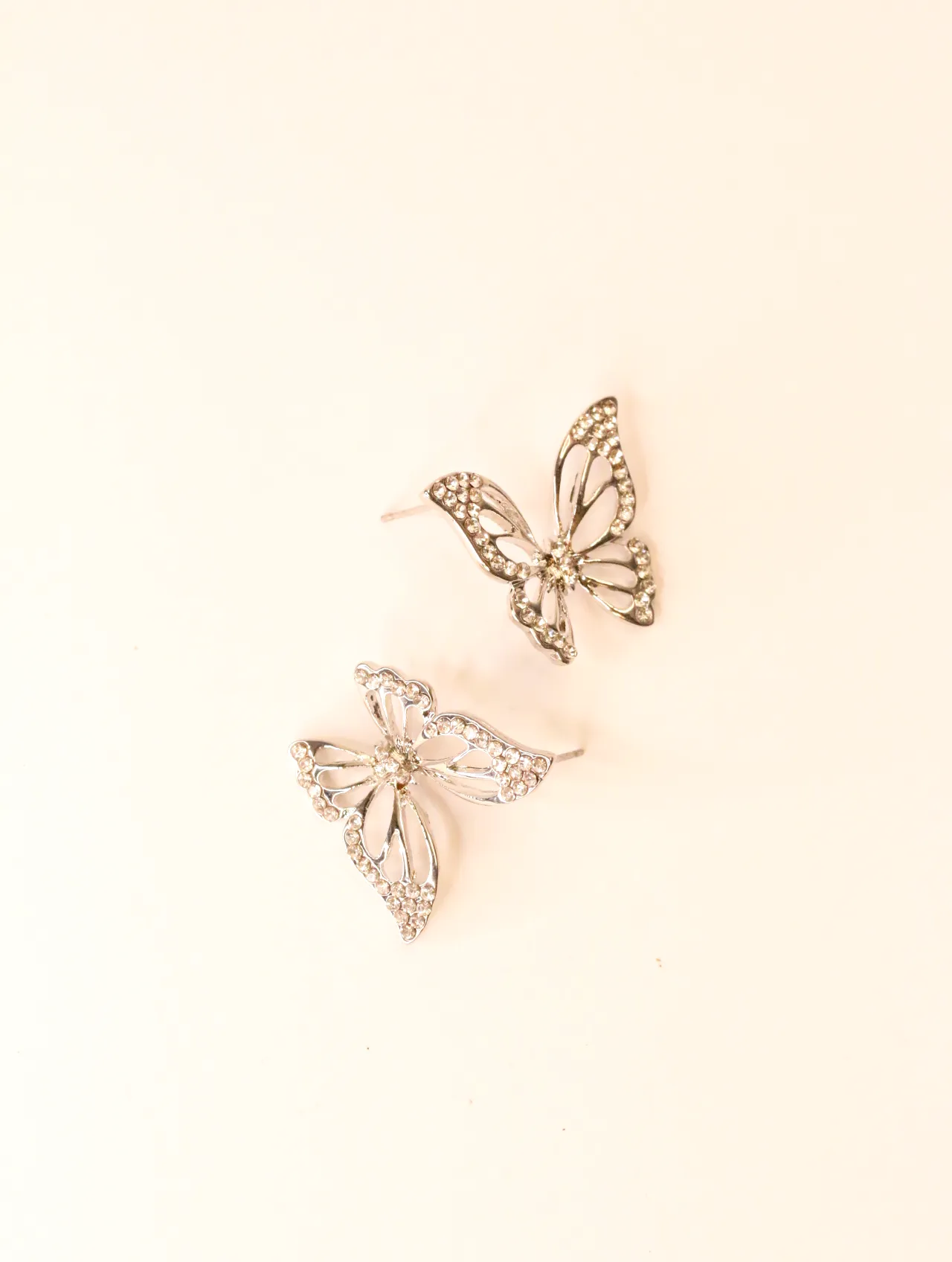 Par de pendientes de botón de mariposa tono plata con pedrería transparente, vistos desde un ángulo ligero. — pendientes dorados, primer plano · Lola y…