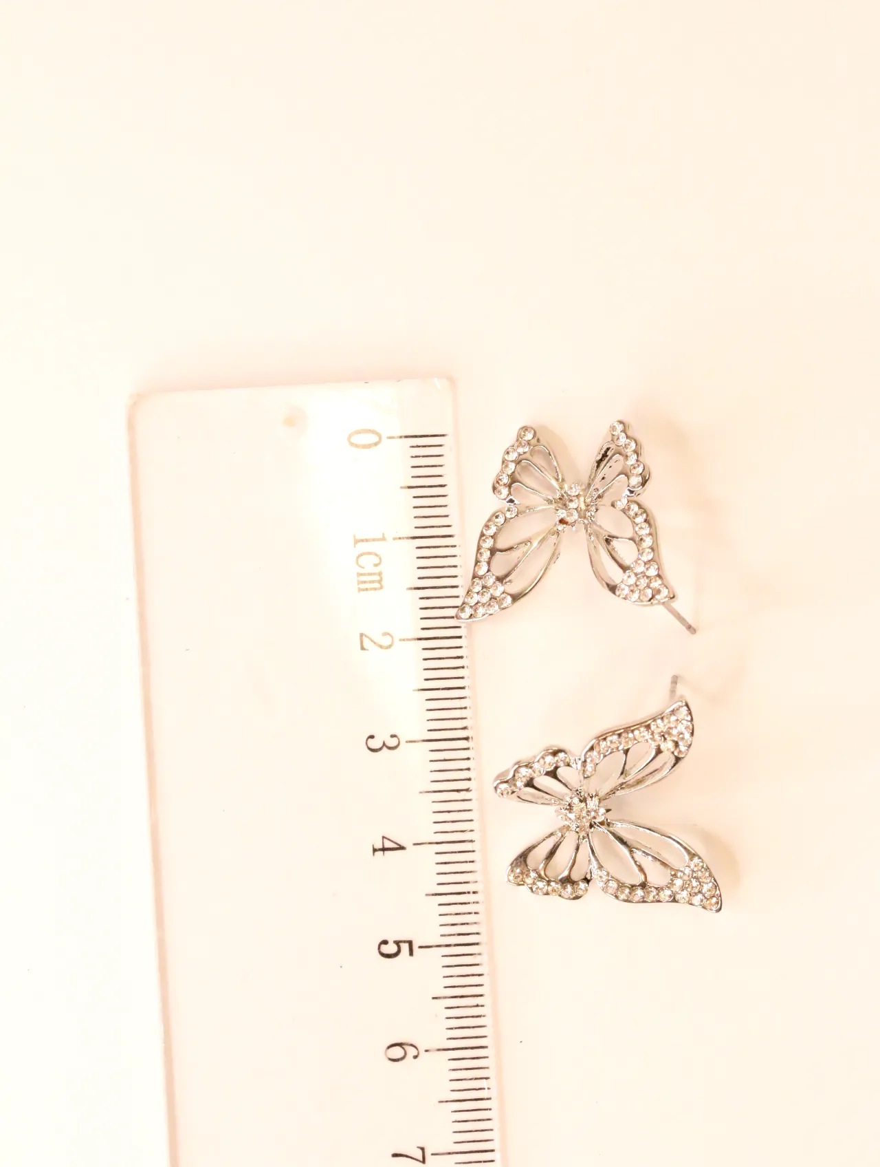Dos pendientes de mariposa junto a una regla que muestra su tamaño, alrededor de 2-2.5 cm. — pendientes de moda, vista lateral · Lola y Sol (BO-PD-050)