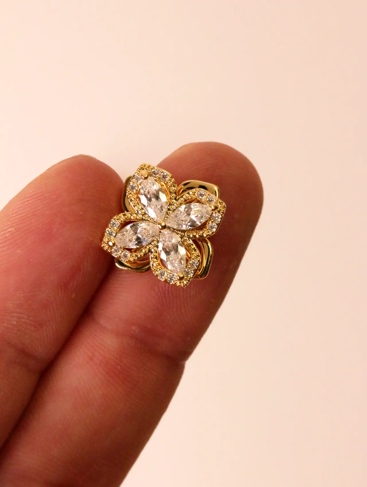 Primer plano de un solo pendiente de trébol brillante en tono dorado con piedras transparentes, sostenido suavemente por los dedos. — pendientes baratos…