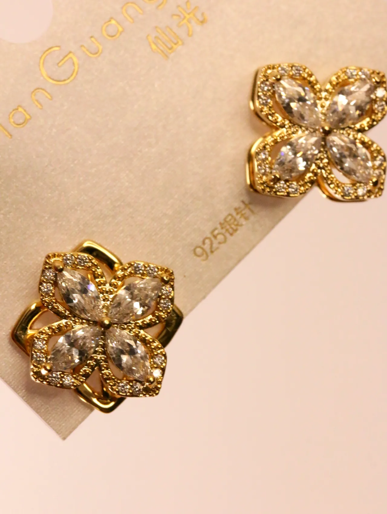 Un par de deslumbrantes pendientes de trébol tono dorado con cristales transparentes, presentados sobre un fondo claro. — pendientes de moda, vista late…