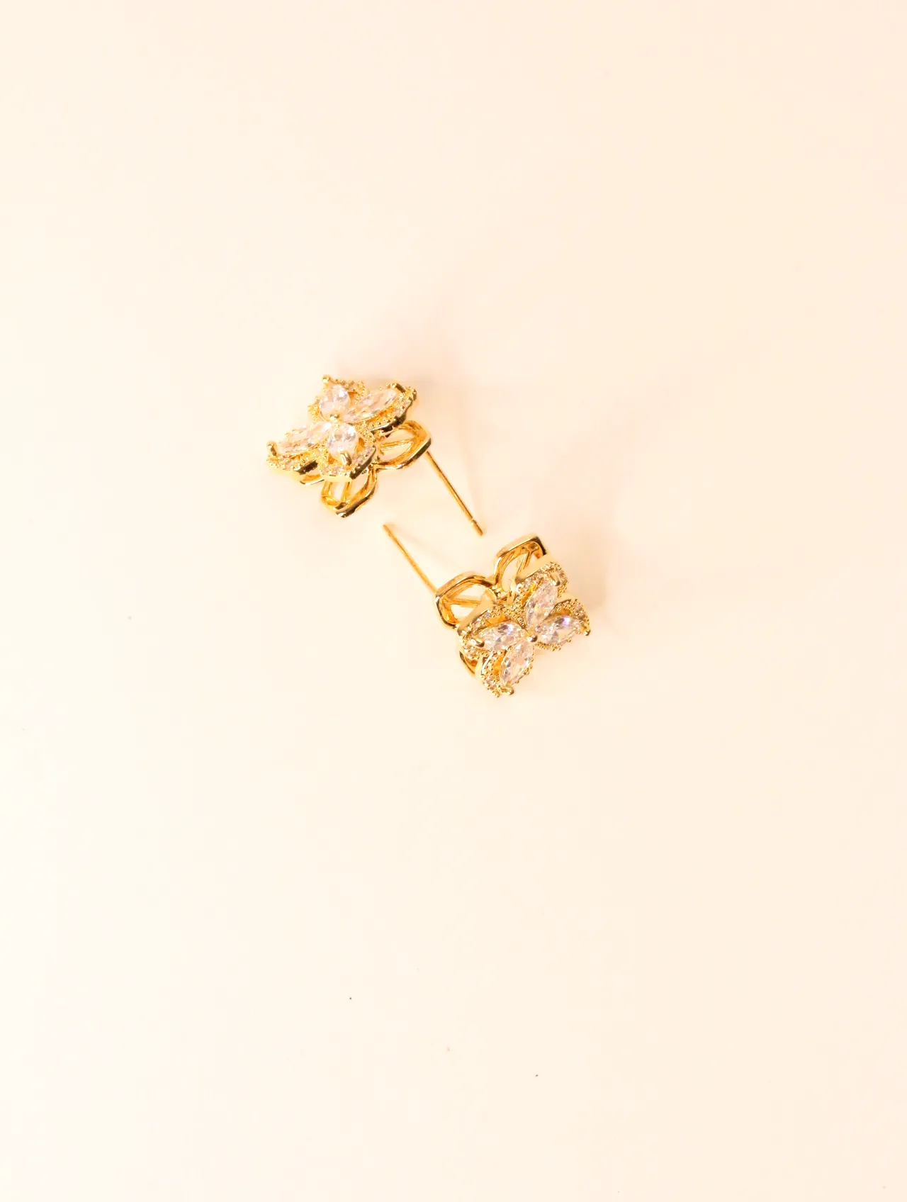 Vista superior de dos pendientes de trébol tono dorado con piedras transparentes, mostrando su diseño completo. — pendientes online, vista principal · L…