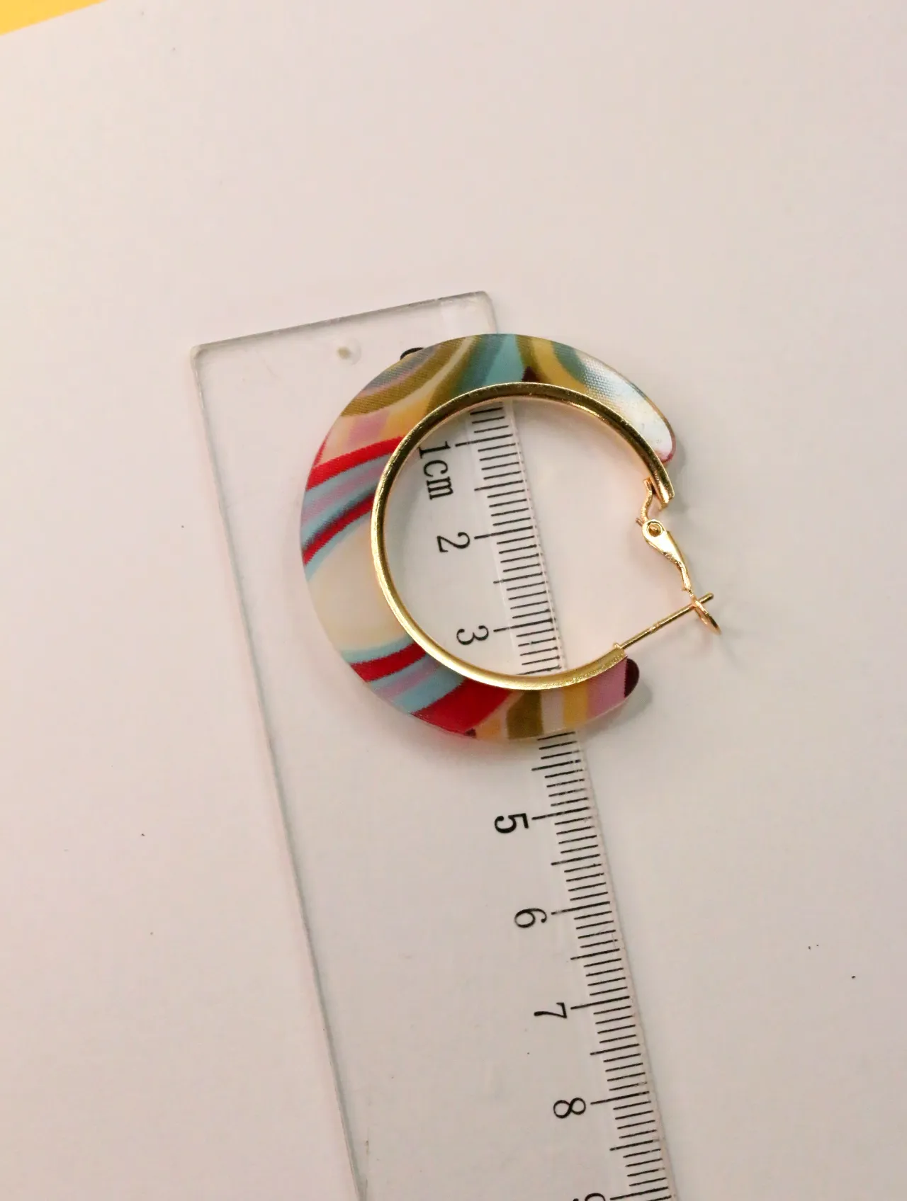Pendiente de aro multicolor junto a una regla — pendientes baratos, detalle · Lola y Sol (CLR-HPS-002)