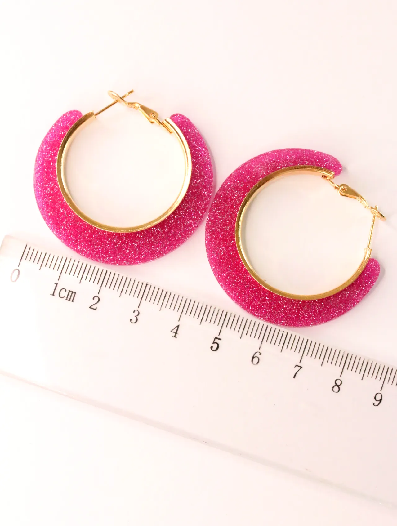 Pendientes de aro con purpurina fucsia junto a una regla — pendientes baratos, detalle · Lola y Sol (CLR-HPS-012)