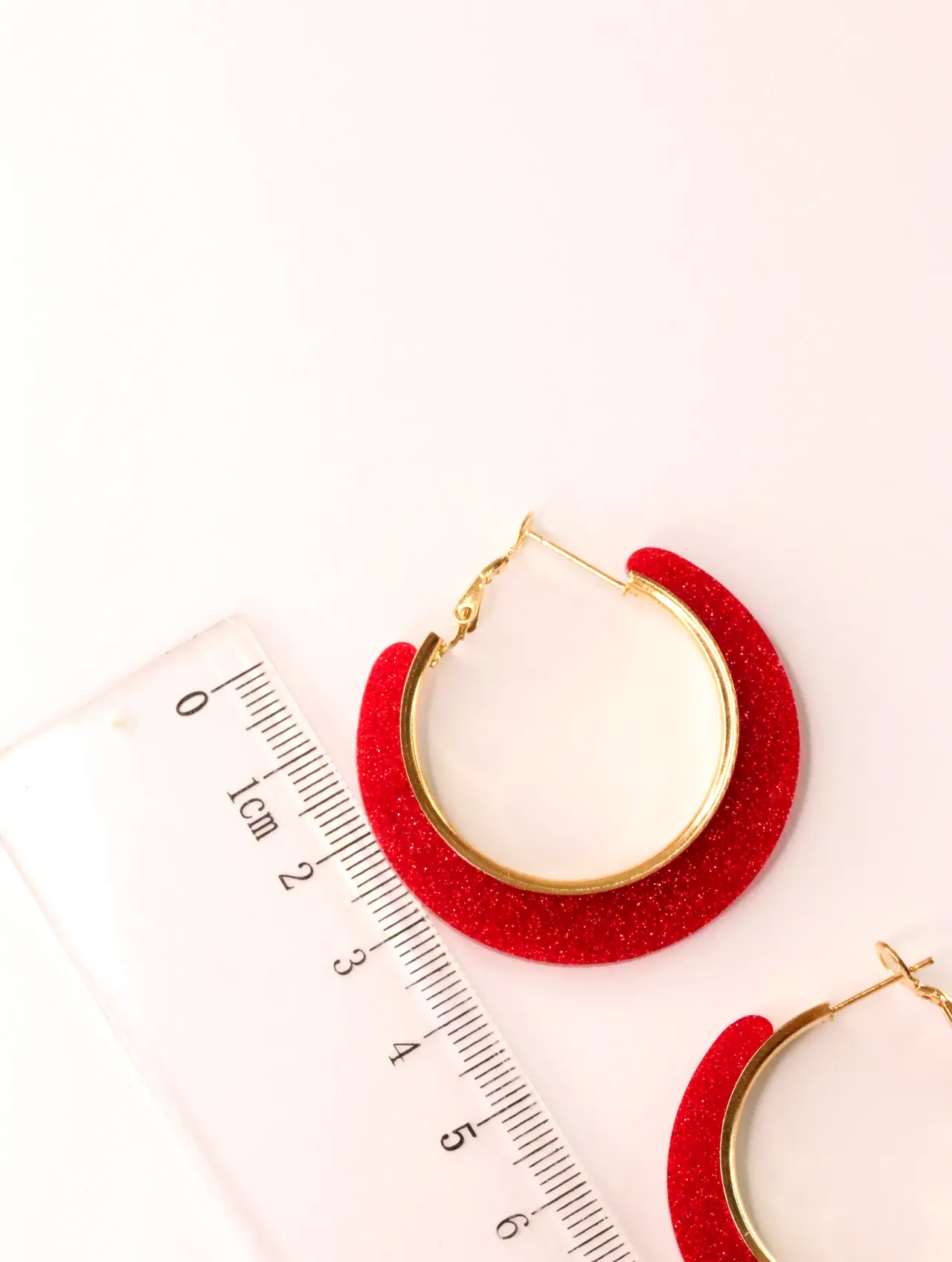 Detalle de pendiente de aro con purpurina roja junto a una regla — pendientes baratos, detalle · Lola y Sol (CLR-HPS-013)