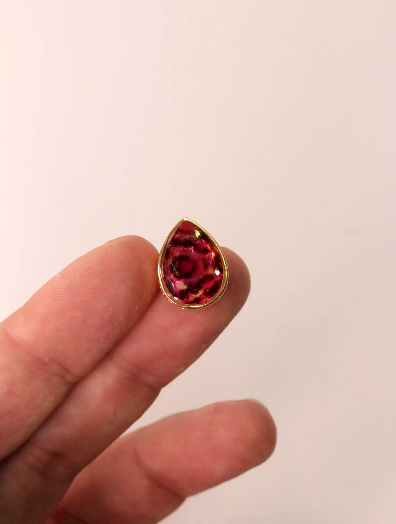 Primer plano de un pendiente de gota con una gema rosa vibrante, sostenido entre dedos. — pendientes baratos, detalle · Lola y Sol (EAR-002)