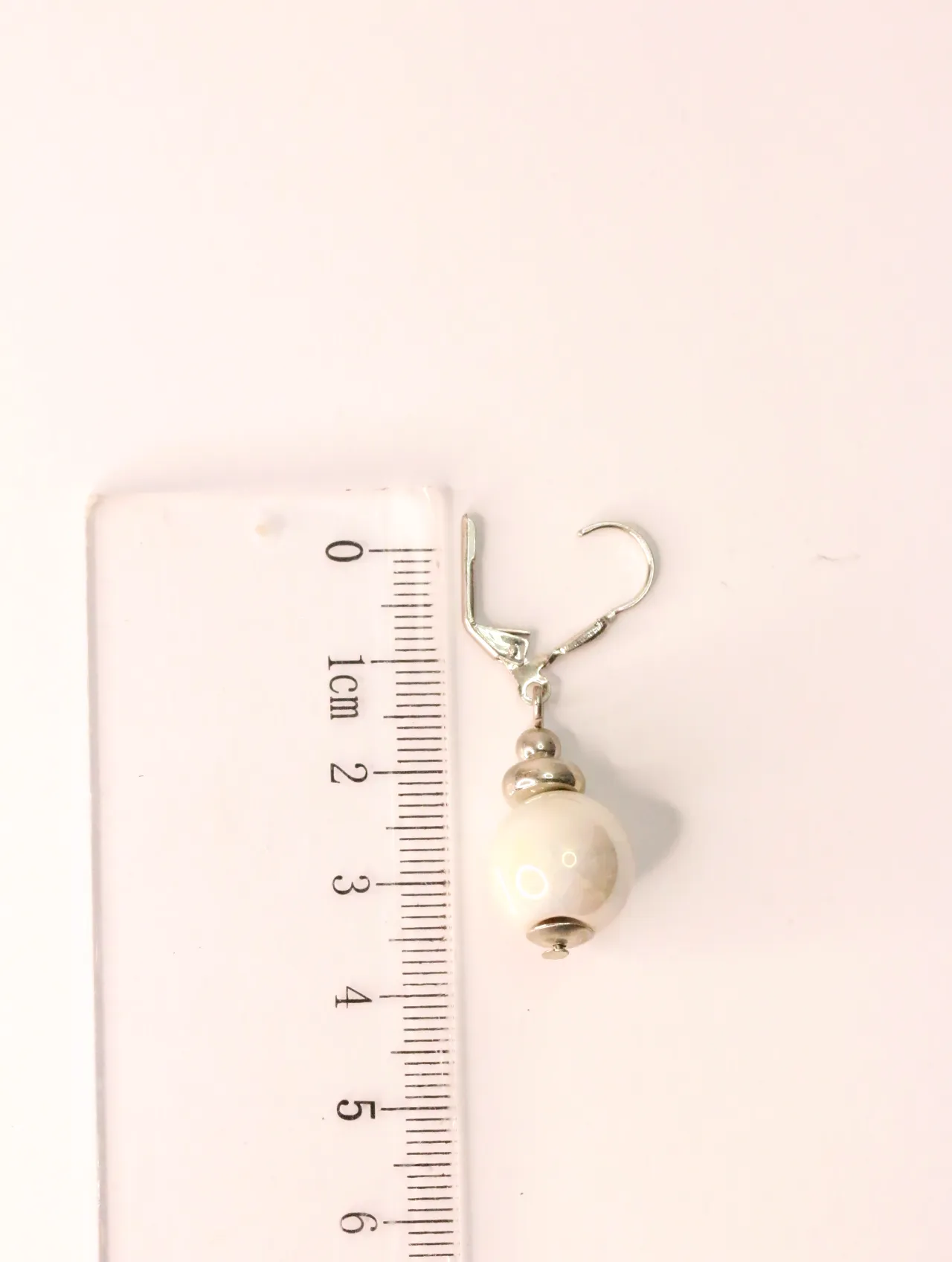 Pendiente largo elegante individual con cuenta de cerámica junto a una regla para referencia de tamaño — pendientes dorados, primer plano · Lola y Sol (…