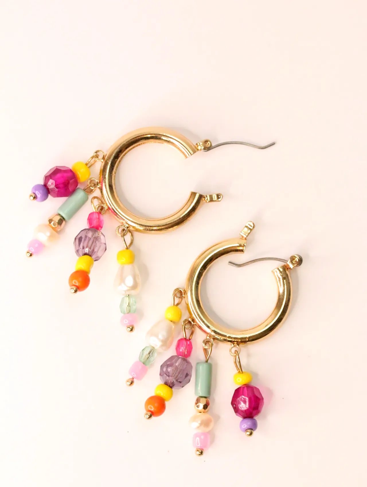 Un par de pendientes de aro dorados adornados con diversas cuentas de colores, sobre un fondo claro. — pendientes para mujer, vista principal · Lola y S…