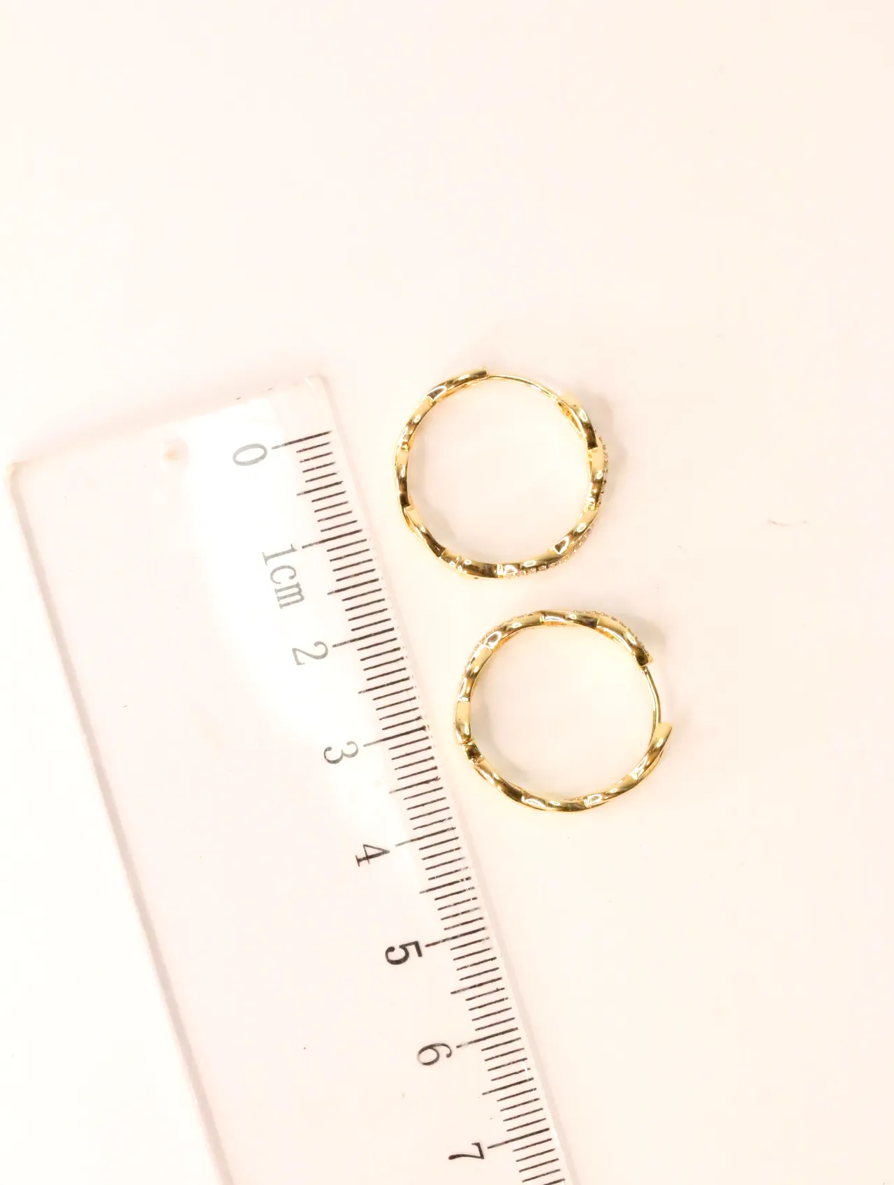 Pendientes de aro dorados entrelazados junto a una regla medidora — pendientes baratos, detalle · Lola y Sol (EAR-016)