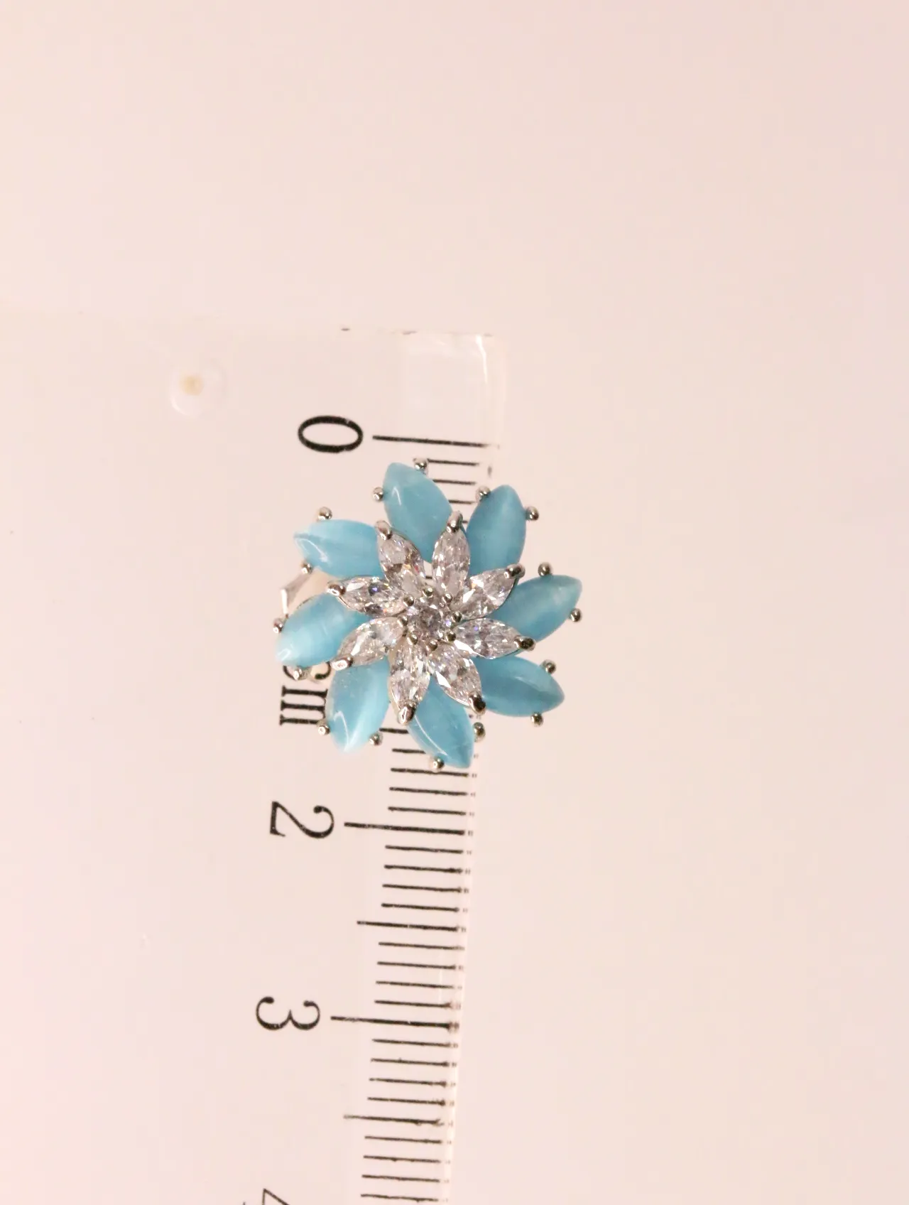 Pendiente floral en tono azul celeste junto a regla de medir — pendientes baratos, detalle · Lola y Sol (EAR-021)