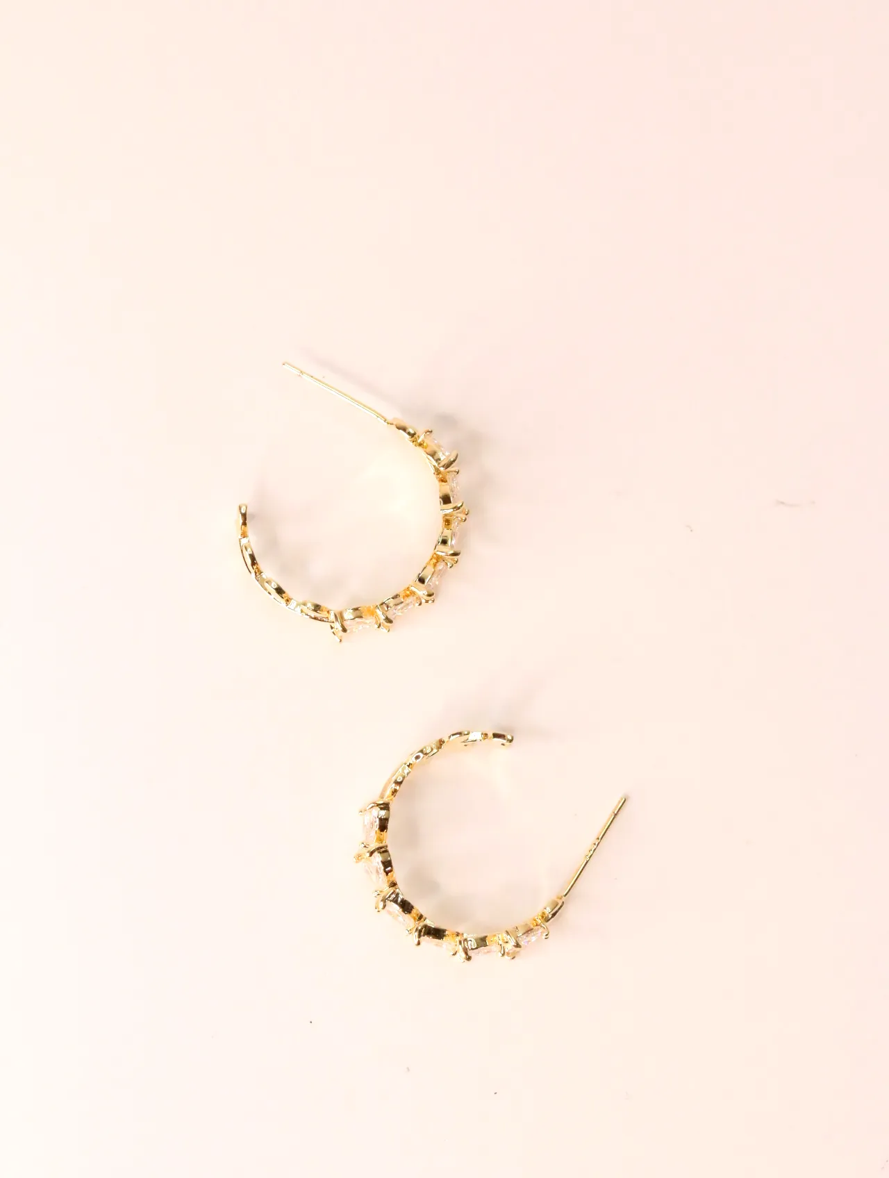 Pareja de pendientes de aro abiertos dorados con circonitas sobre fondo rosa claro — pendientes para mujer, vista principal · Lola y Sol (EAR-022)