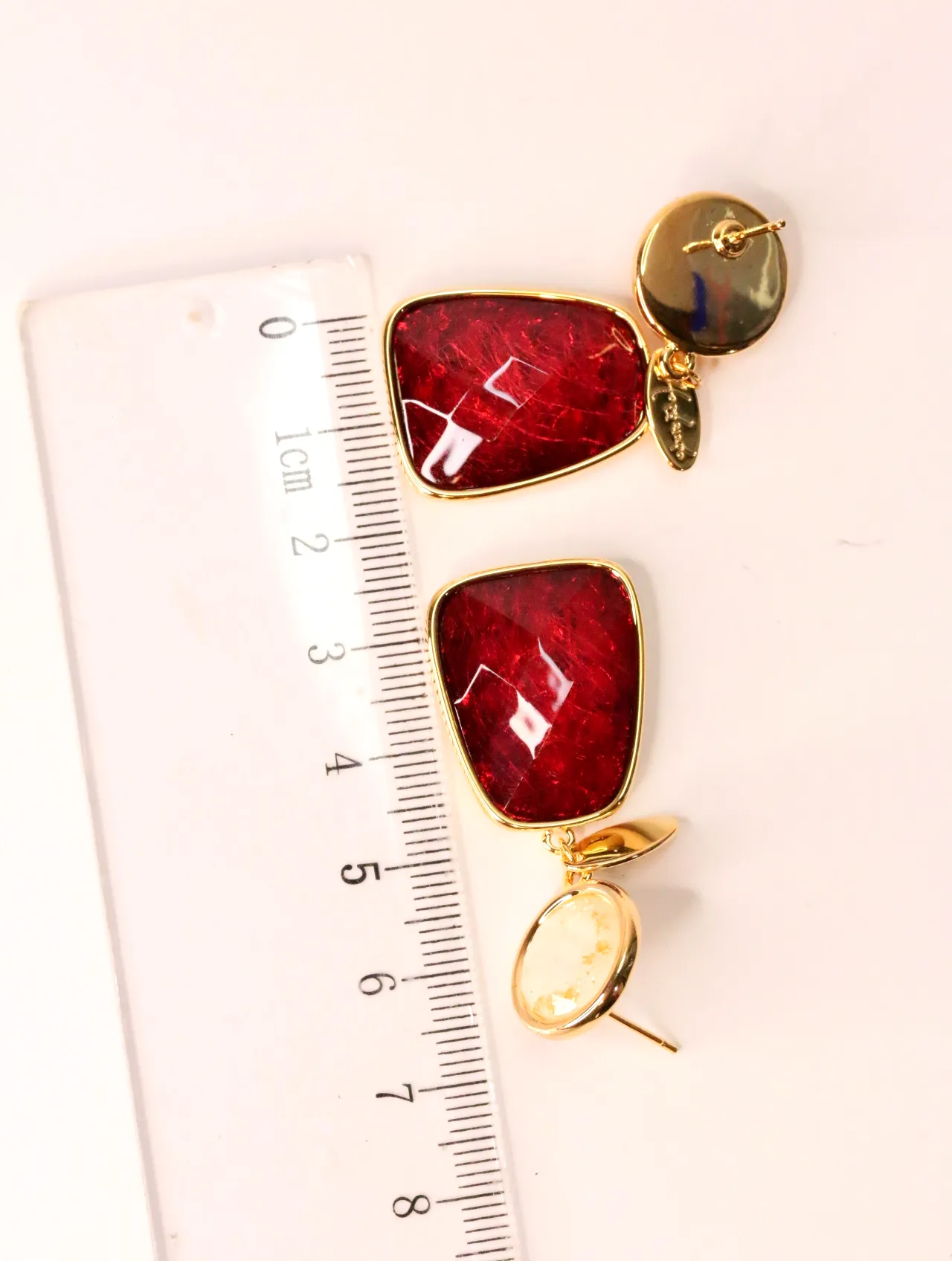 Pendientes dorados con piedras rojas facetadas junto a una regla de medir — pendientes para mujer, vista principal · Lola y Sol (EAR-023)
