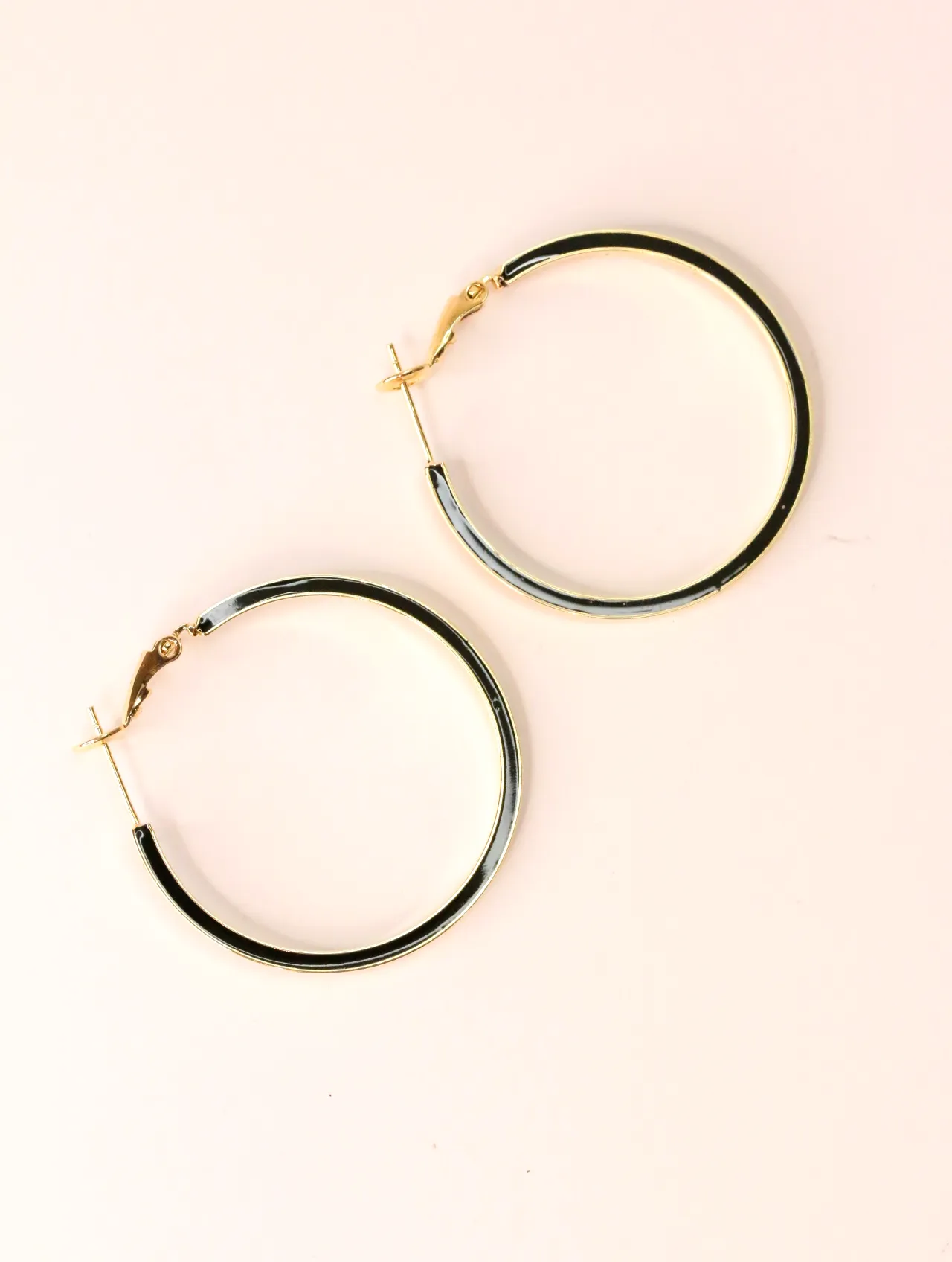 Pareja de pendientes de aro dorados con esmalte negro sobre fondo blanco — pendientes originales, detalle del acabado · Lola y Sol (EAR-033)