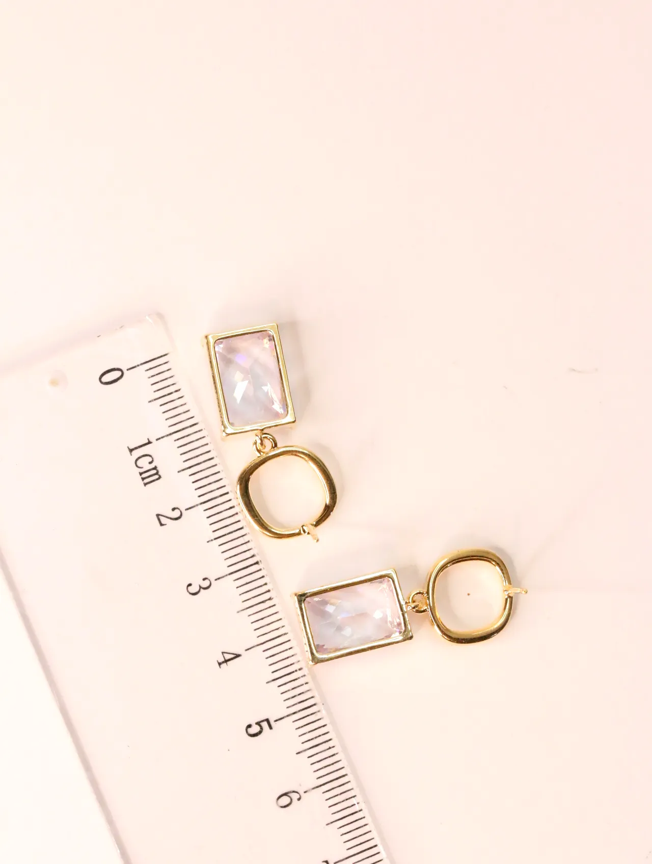 Pendientes dorados con cristal rectangular junto a una regla de medición — pendientes dorados, primer plano · Lola y Sol (EAR-038)