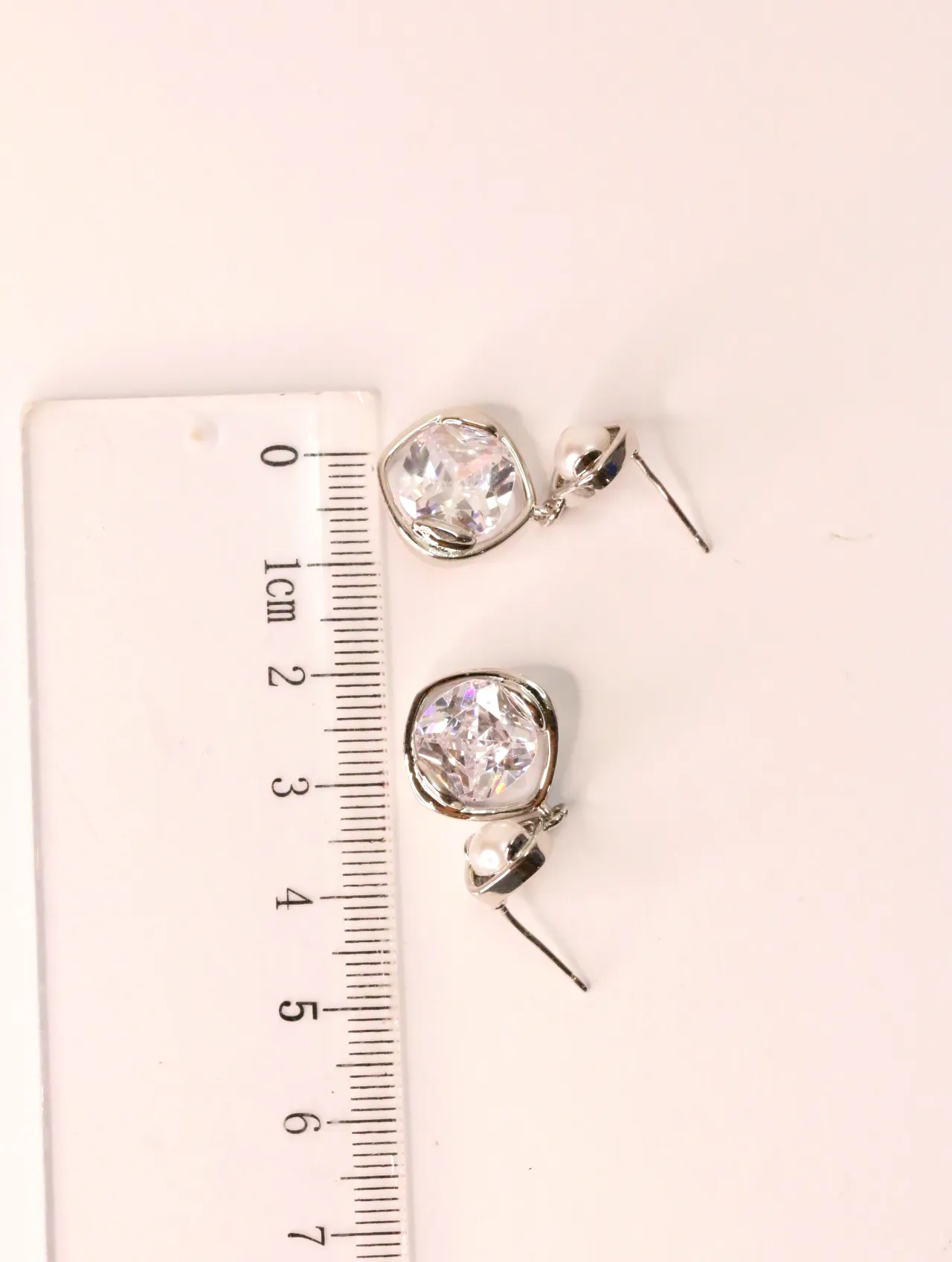 Pendientes de bisutería plateados con cristal junto a una regla milimetrada — pendientes dorados, primer plano · Lola y Sol (EAR-039)