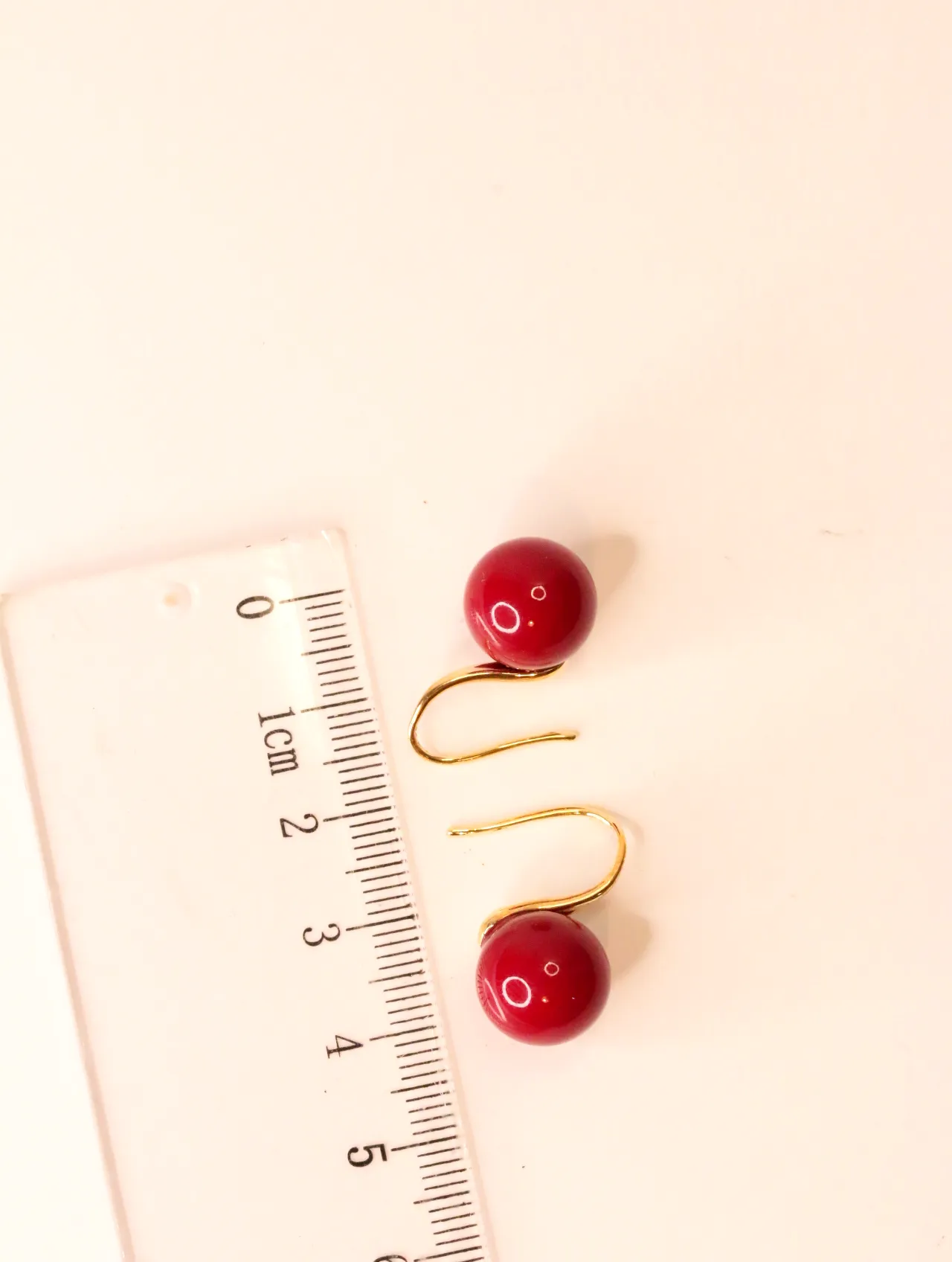 Pendientes con esfera roja medidos junto a una regla — pendientes baratos, detalle · Lola y Sol (EAR-045)
