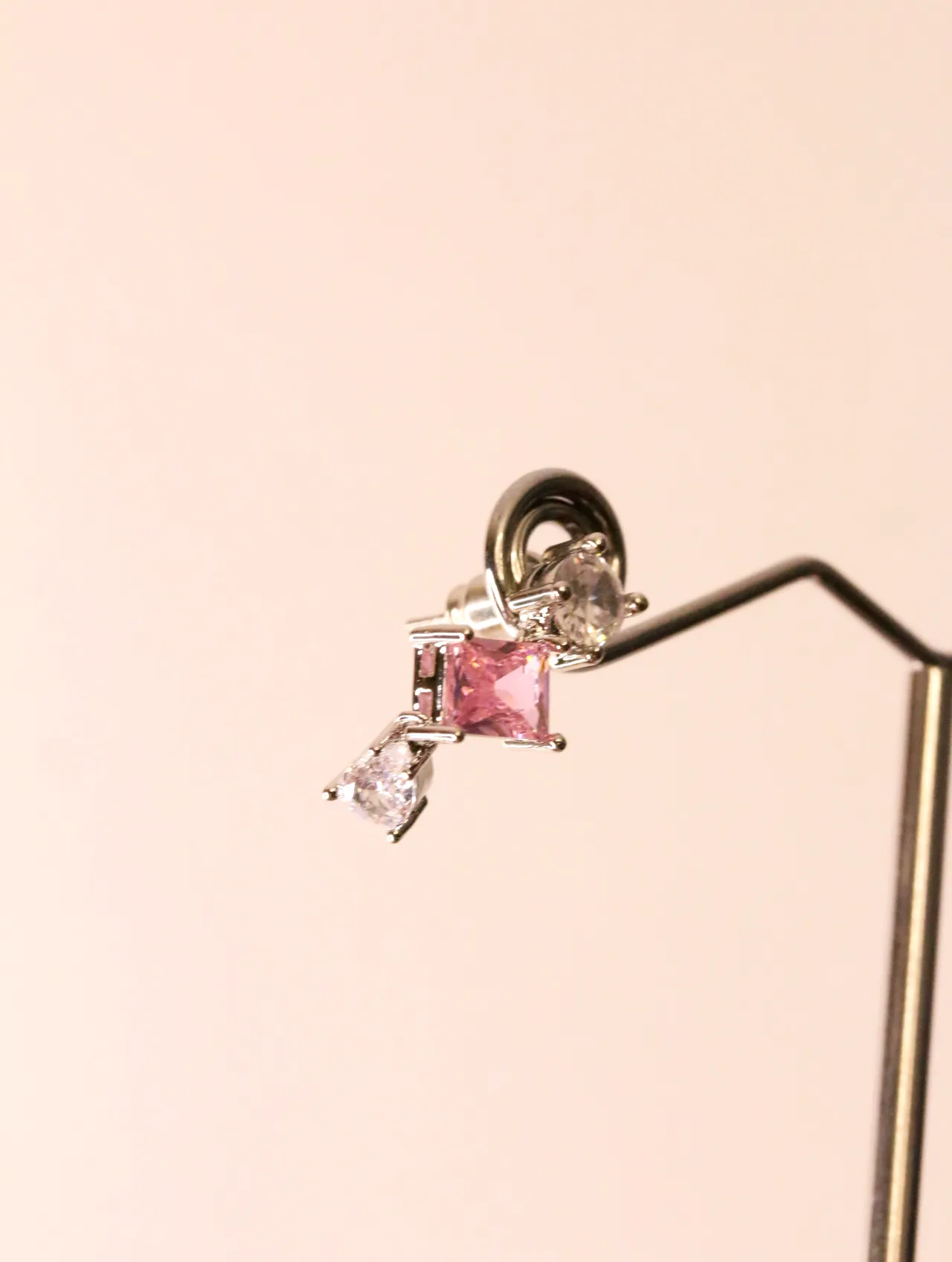 Pendiente con cristal rosa exhibido en soporte metálico para bisutería — pendientes dorados, primer plano · Lola y Sol (EAR-046)