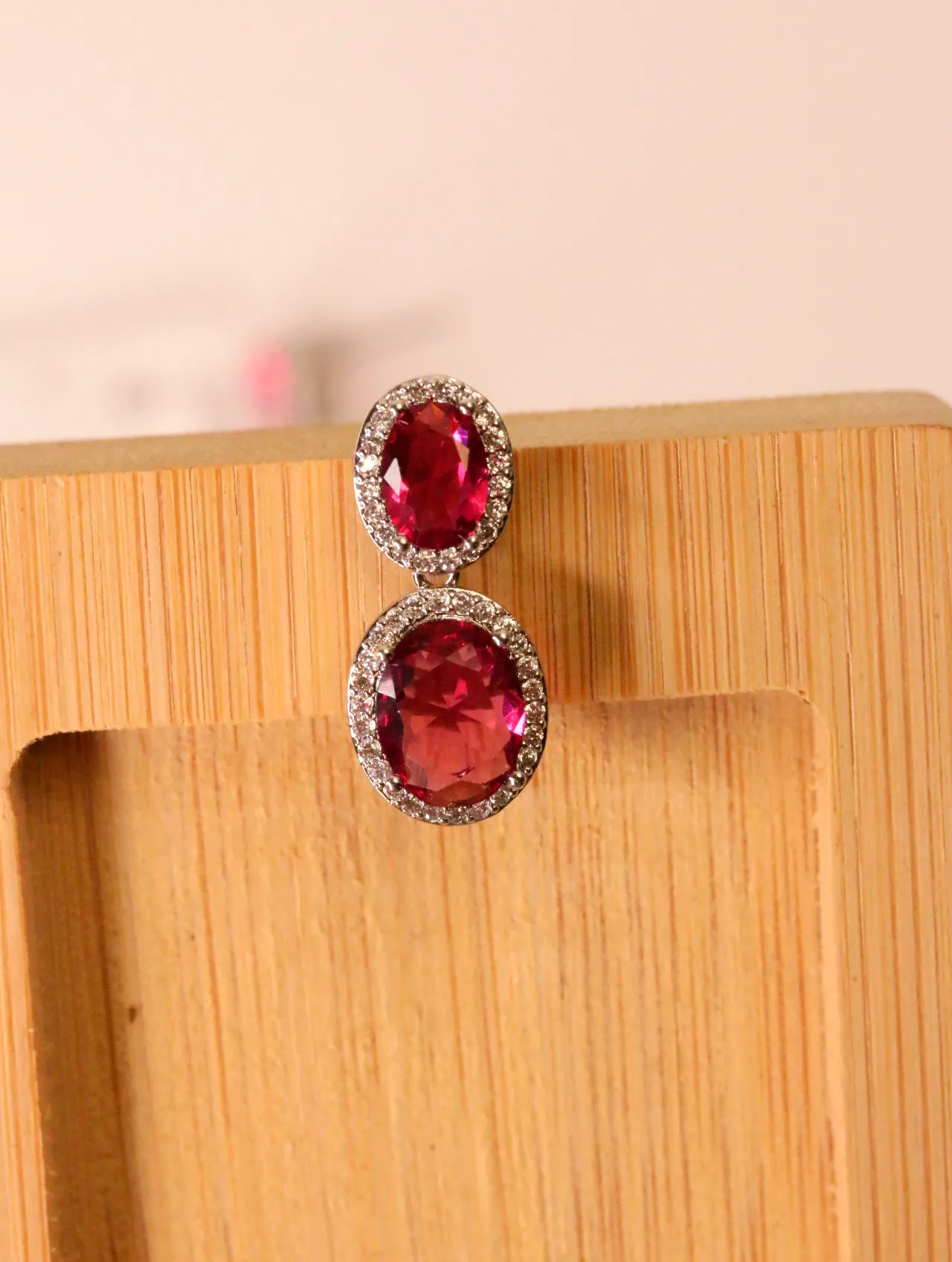 Detalle de pendiente con doble piedra fucsia sobre soporte de madera — pendientes dorados, primer plano · Lola y Sol (EAR-048)