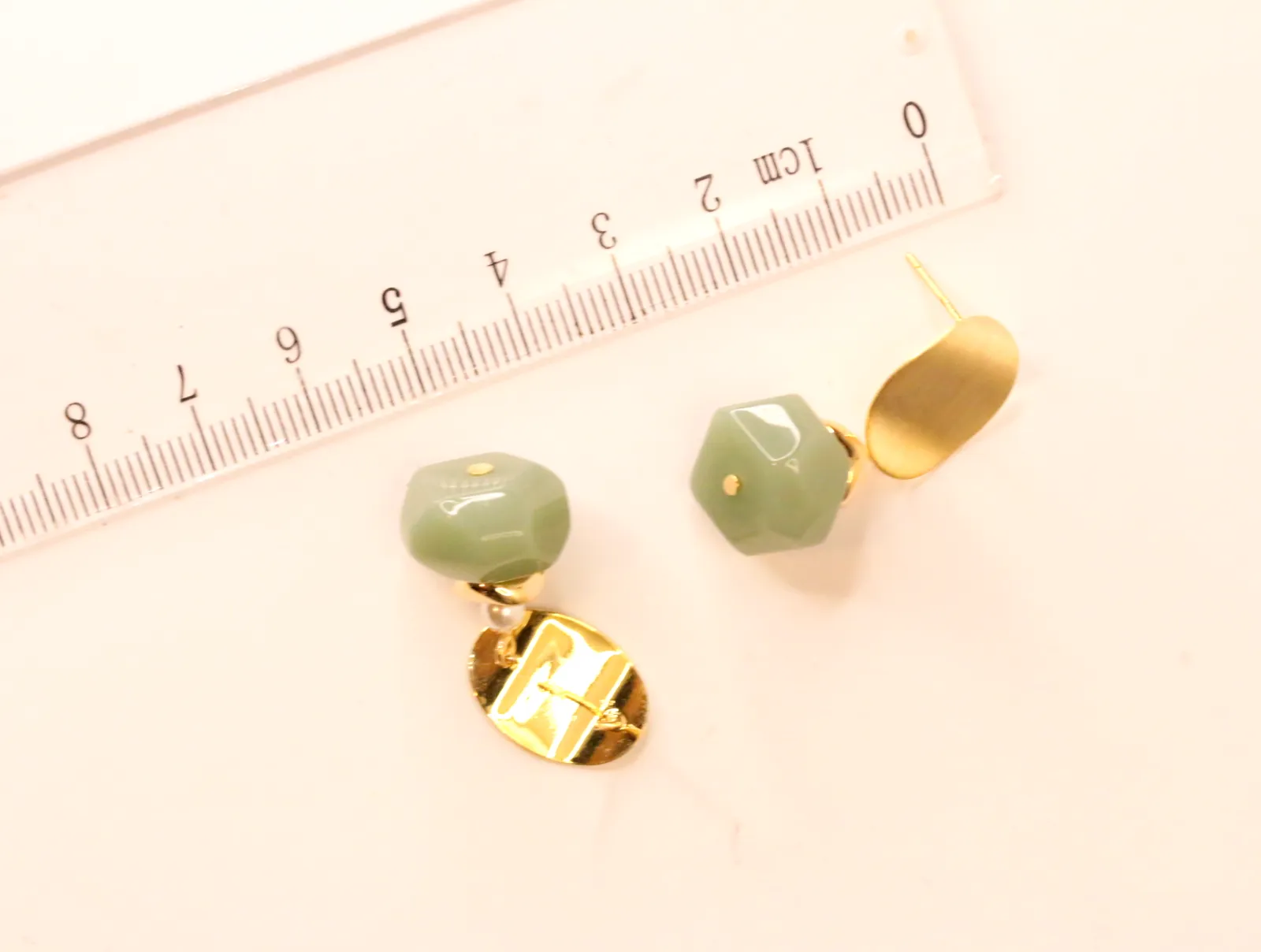 Pendientes colgantes verdes y dorados junto a una regla milimetrada — pendientes dorados, primer plano · Lola y Sol (EAR-050)
