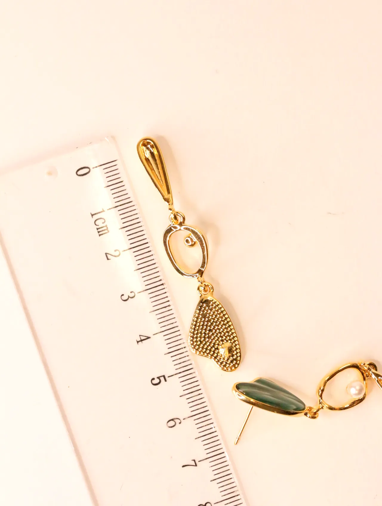Pendientes colgantes dorados situados junto a una regla graduada — pendientes de moda, vista lateral · Lola y Sol (EAR-056)