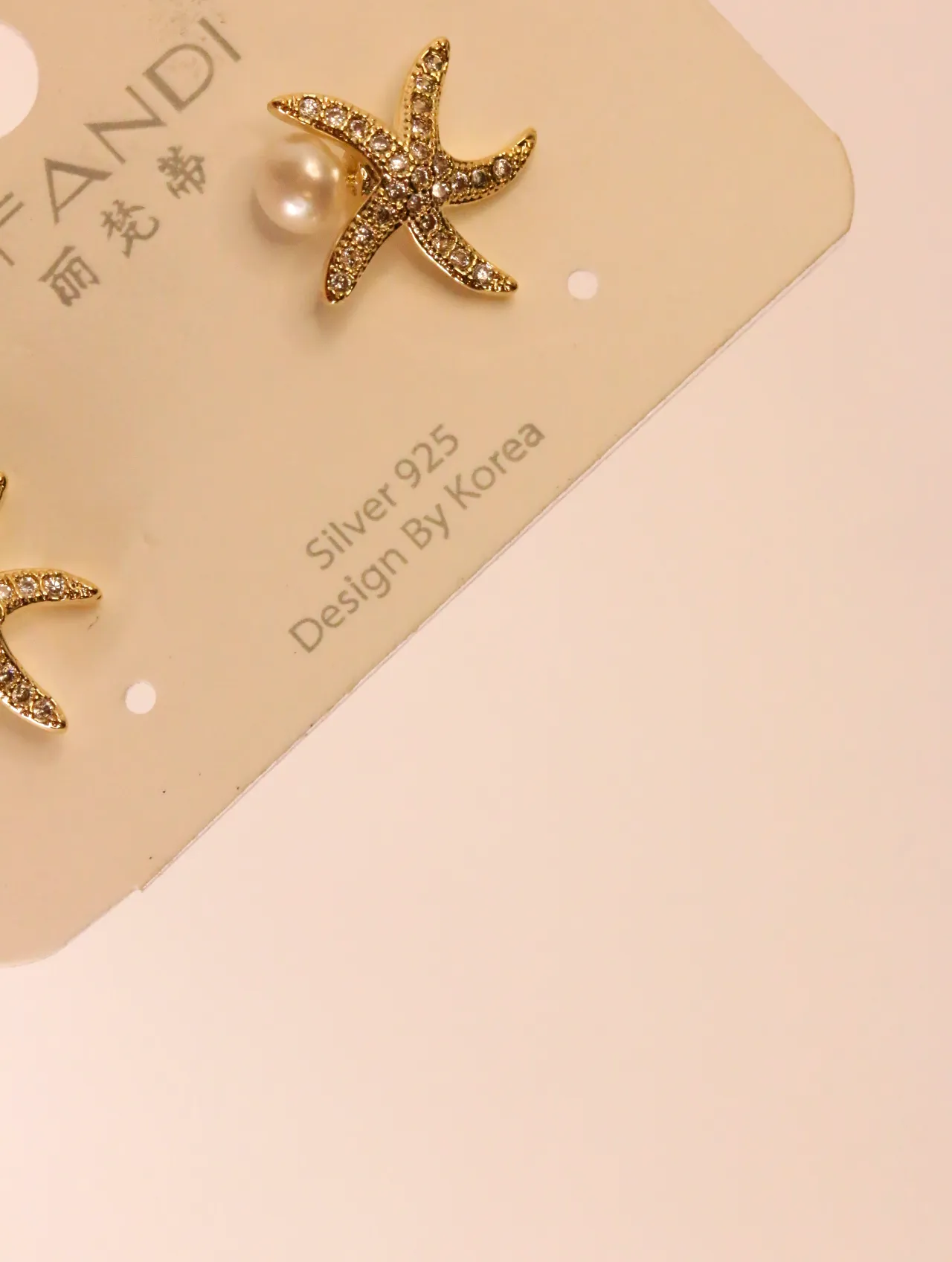 Primer plano de pendiente de estrella de mar dorada con circonitas y perla en soporte — pendientes para mujer, vista principal · Lola y Sol (EAR-062)