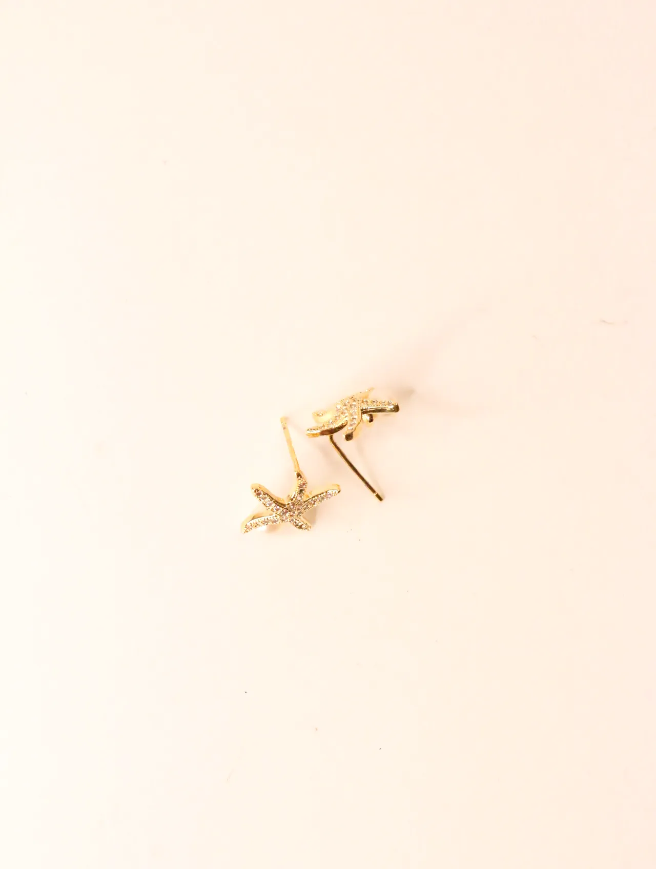 Pendientes de botón en forma de estrella de mar dorada sobre fondo neutro — pendientes dorados, primer plano · Lola y Sol (EAR-062)