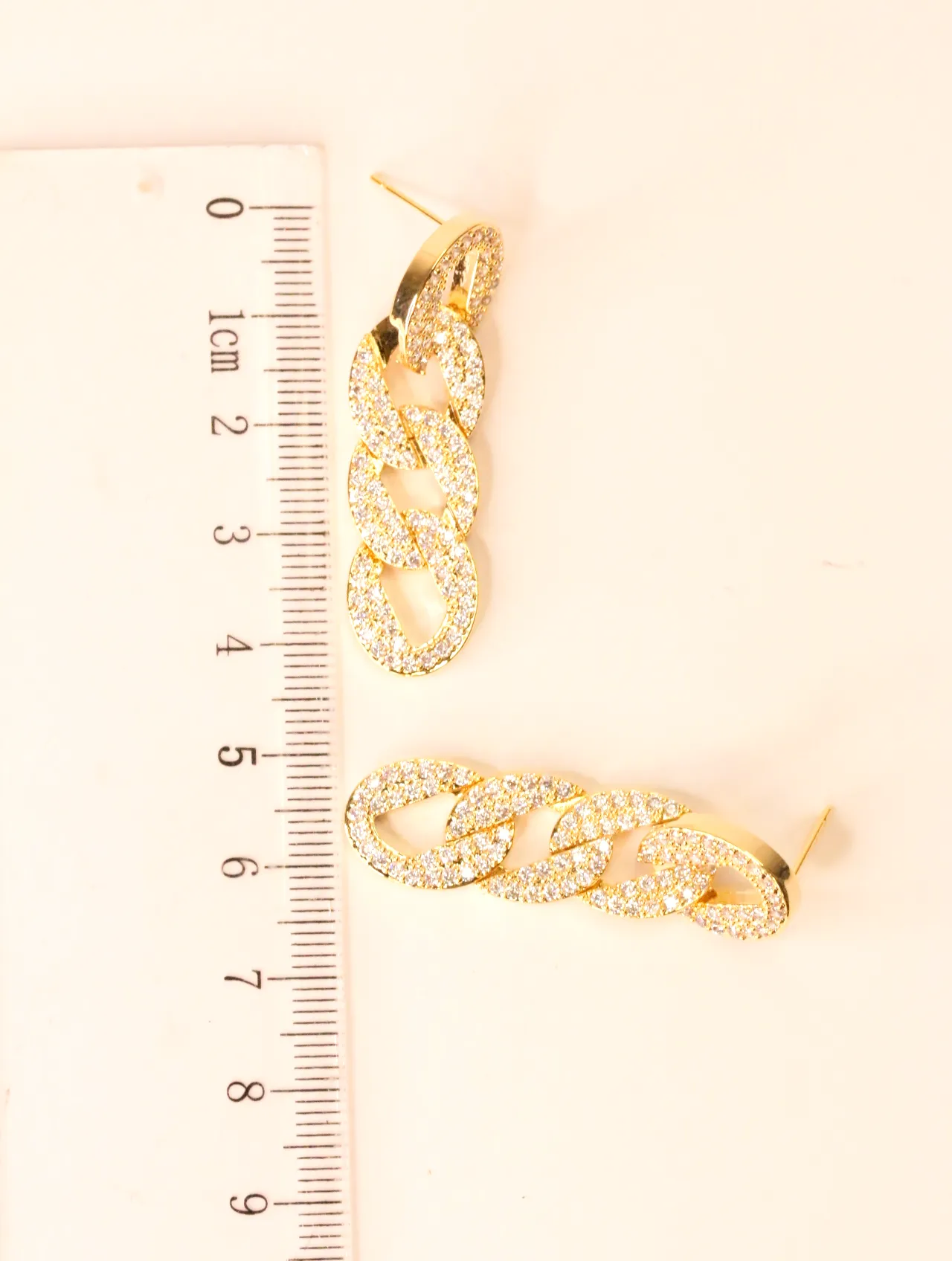 Pendientes dorados de cadena con circonitas junto a una regla — pendientes de moda, vista lateral · Lola y Sol (EAR-064)